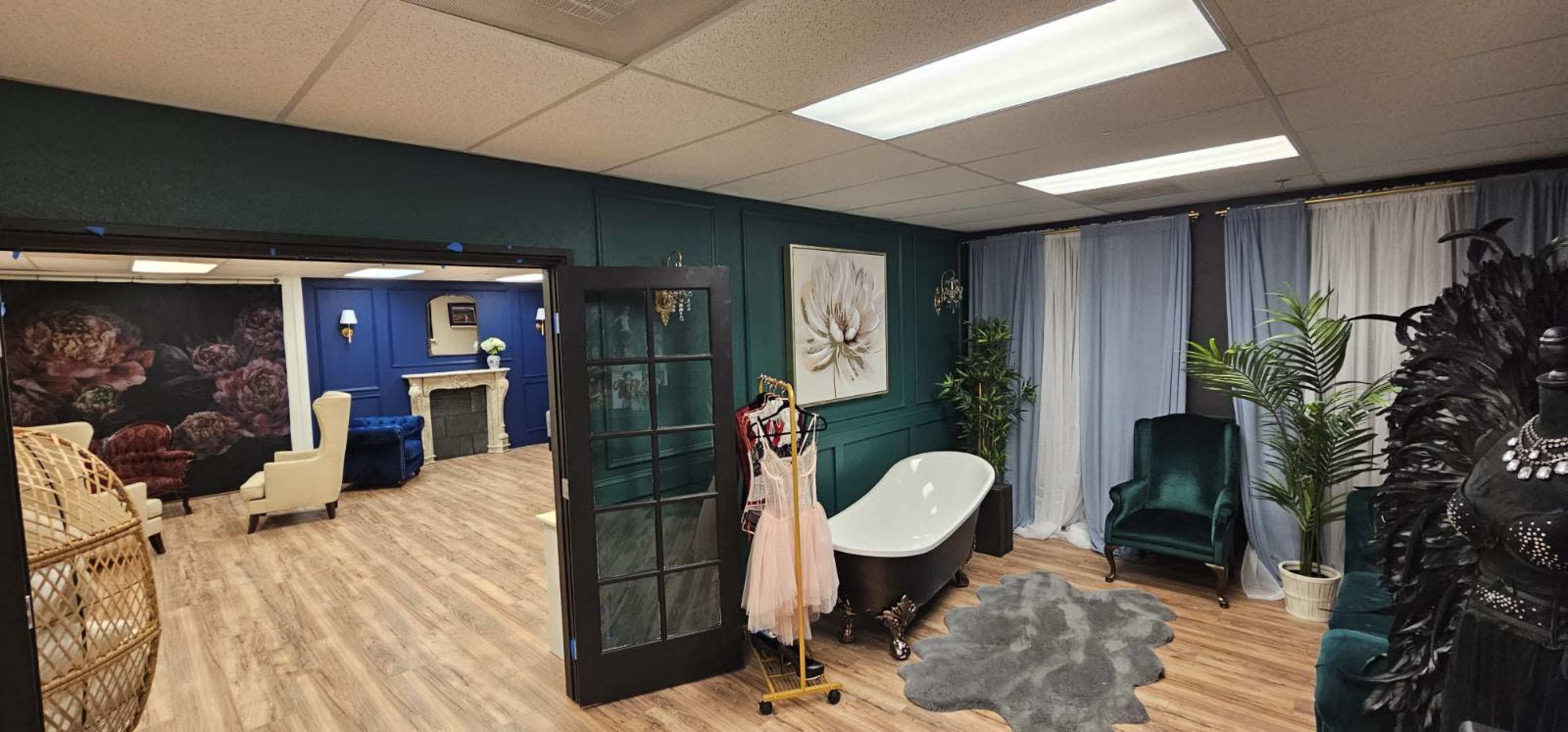 The image shows a stylish interior space featuring a bathtub, a dressing area with clothing displays, and a cozy lounge with seating and decorative plants.