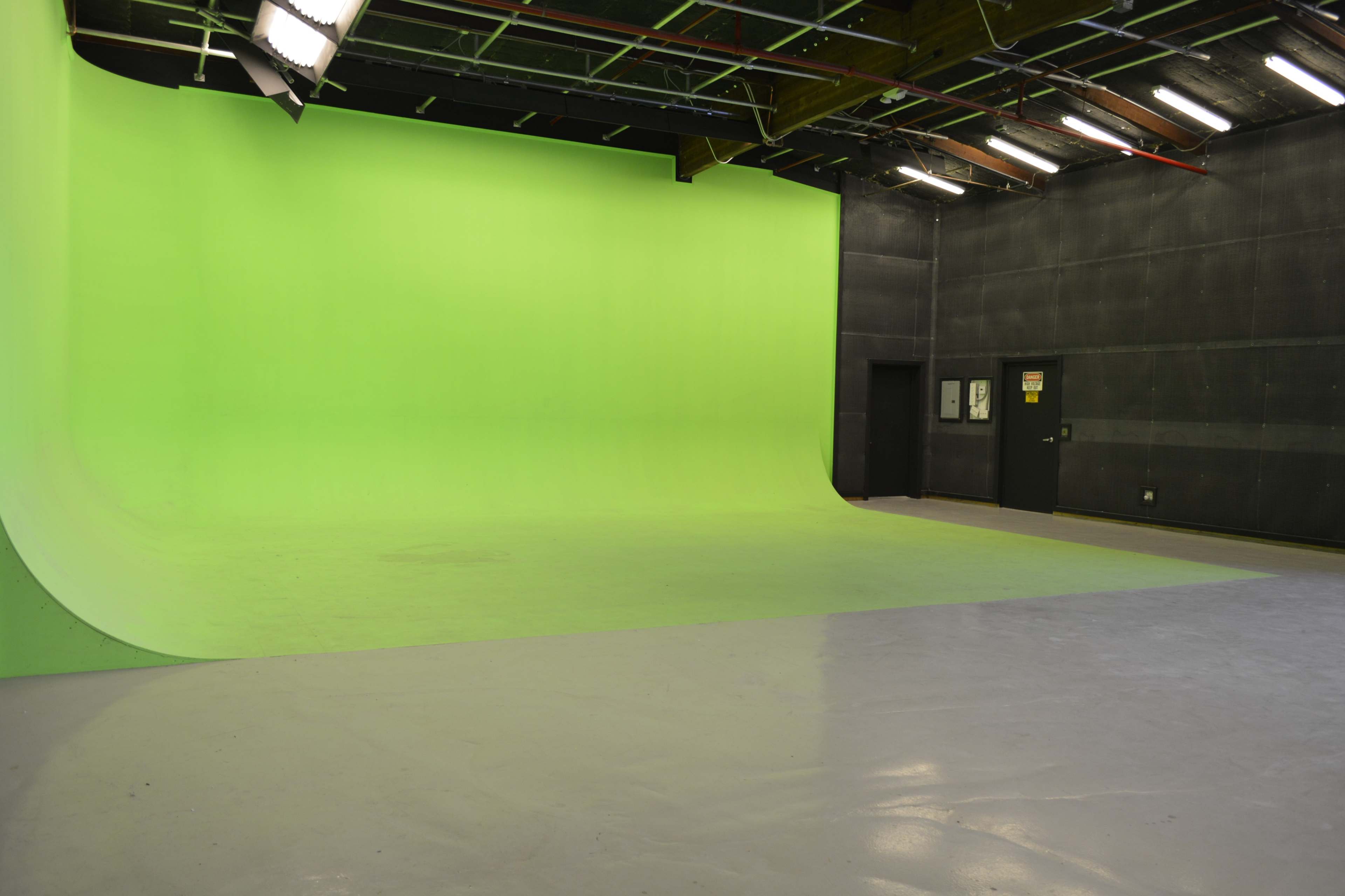 A spacious green screen studio with a curved backdrop and polished gray floor.