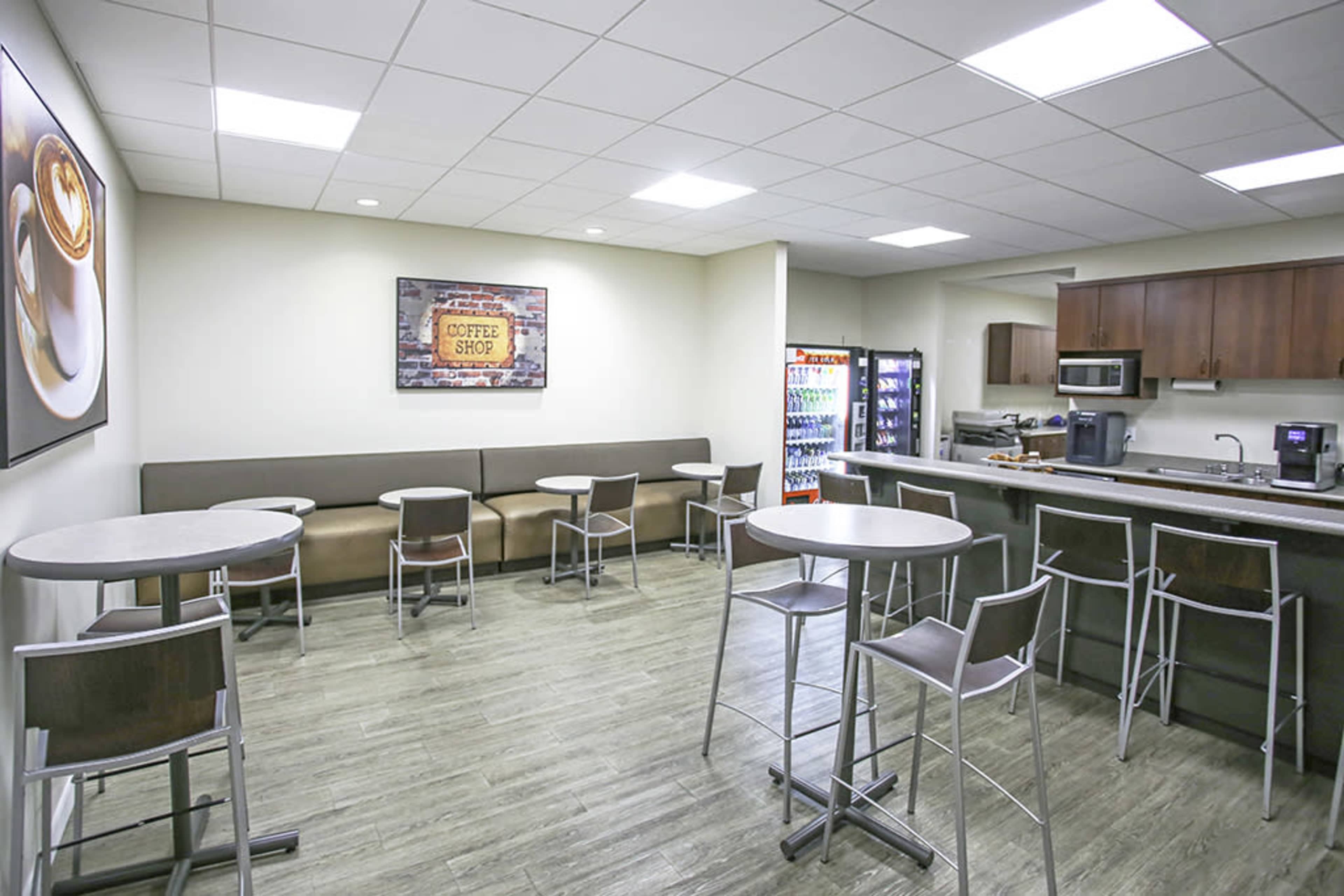 A small coffee shop area with tables and chairs, a vending machine, and a counter with kitchen equipment.