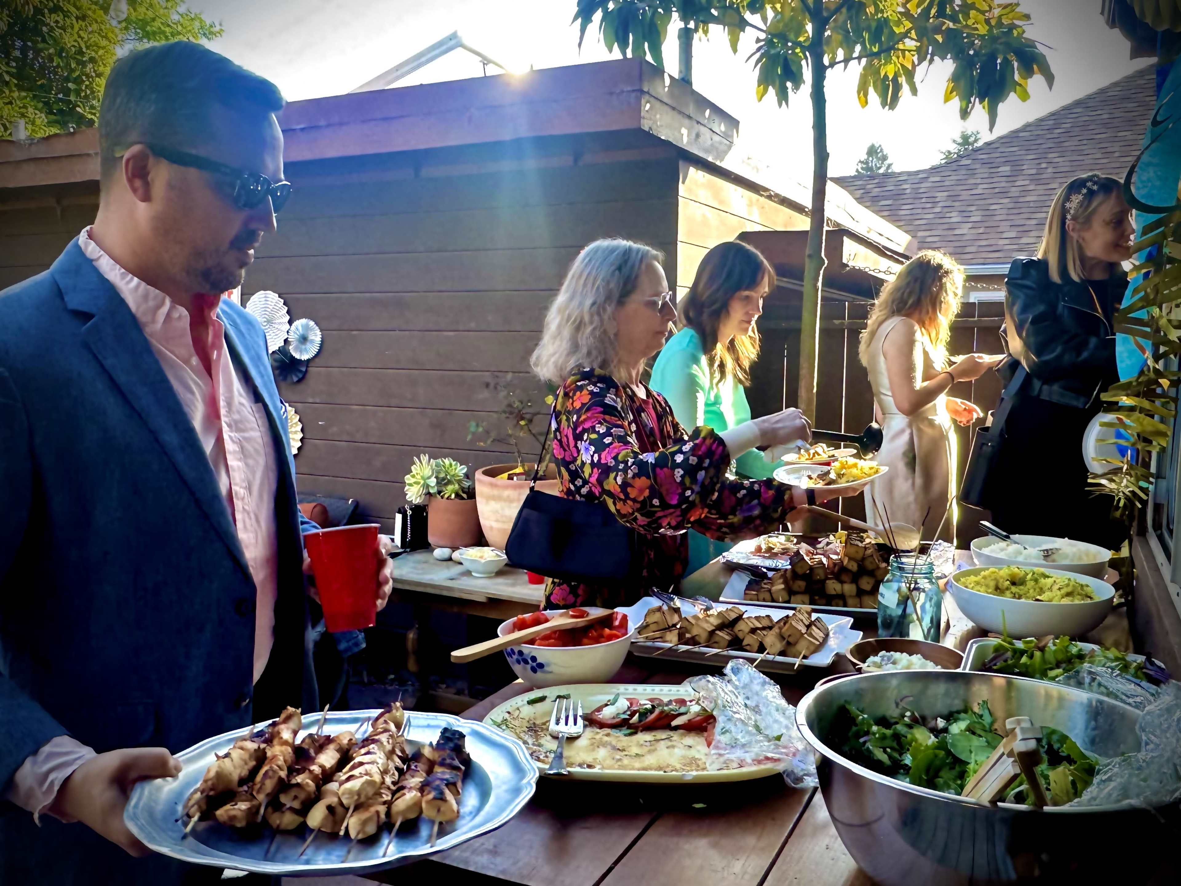 A group of people gathers around a table filled with various dishes, while two individuals serve food onto their plates.