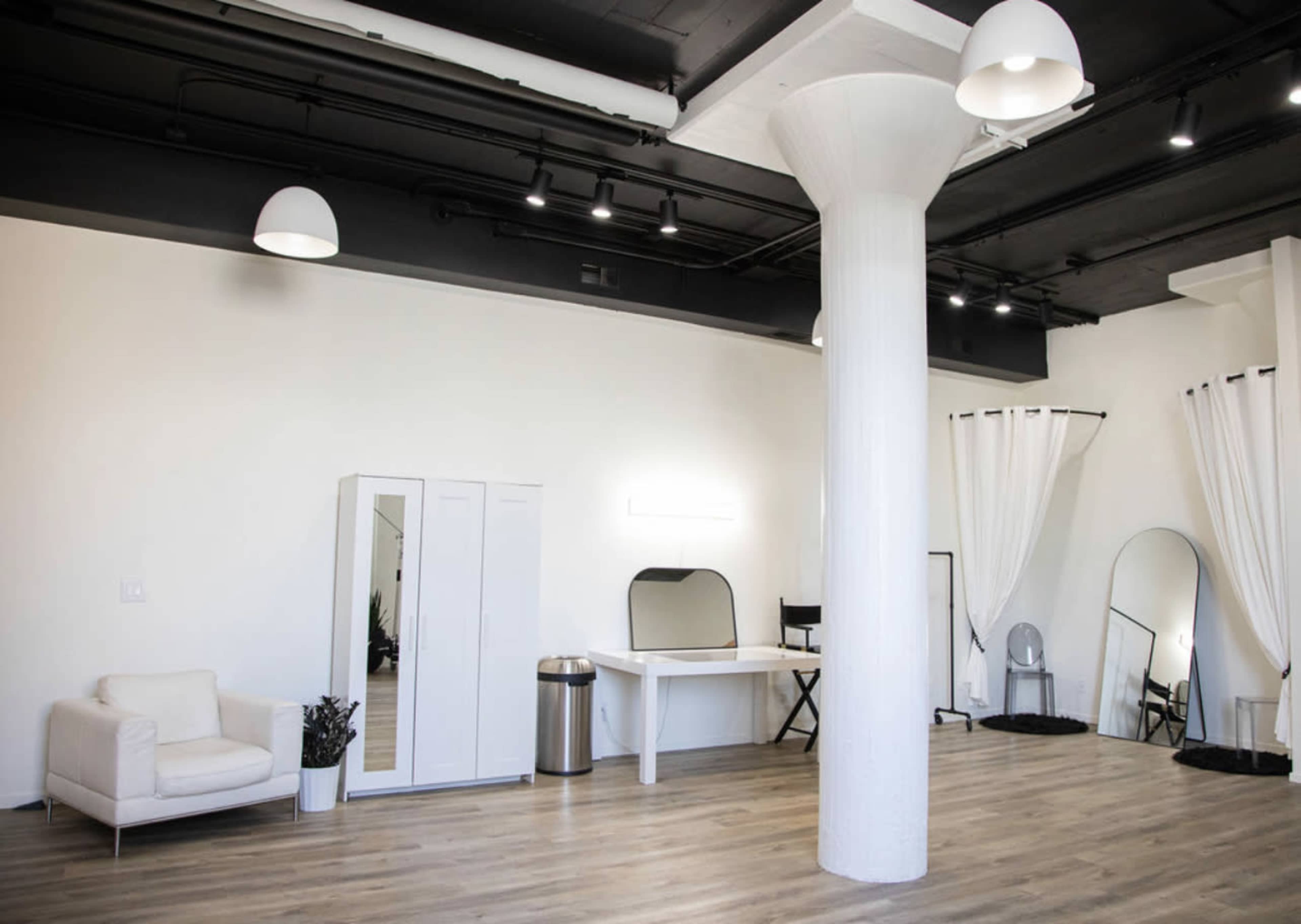 A spacious, minimalist interior featuring a white sofa, a tall column, a dressing table, and several mirrors.
