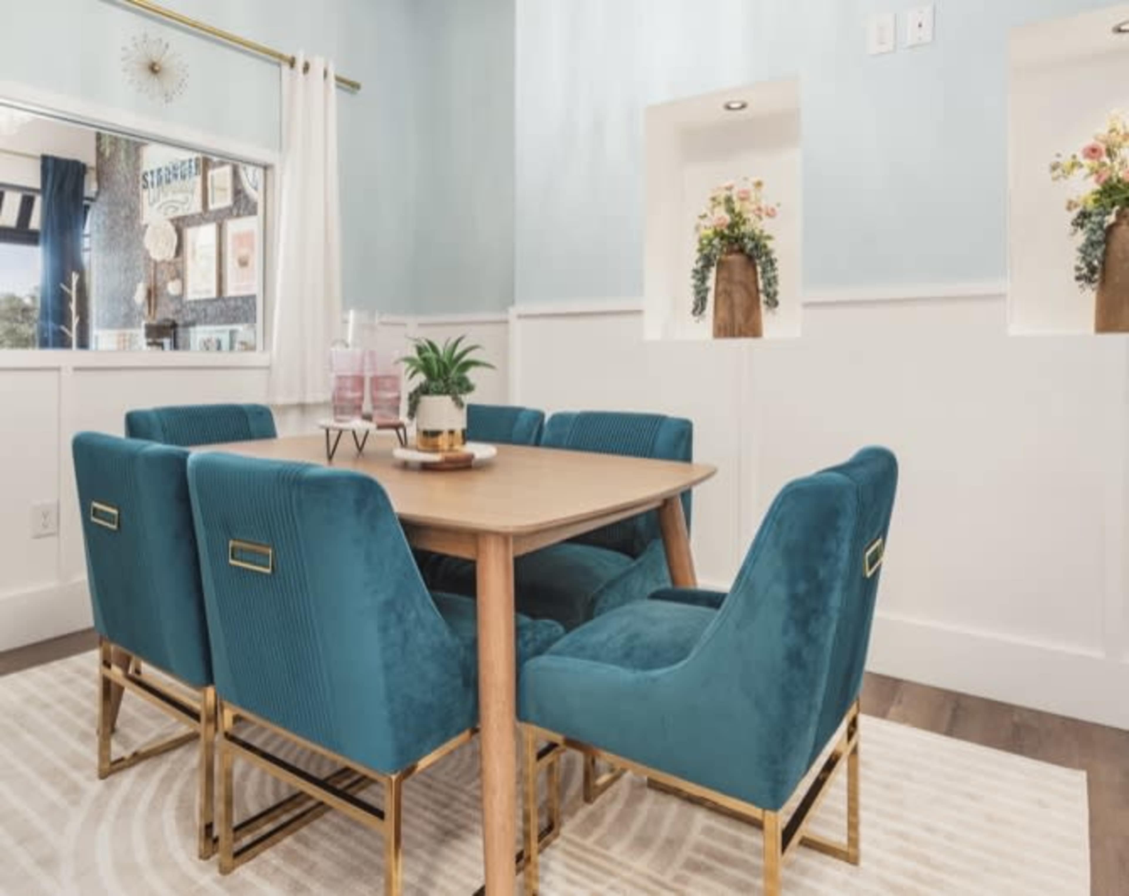 A dining area with a wooden table surrounded by six blue velvet chairs and decorated with potted plants on the walls.