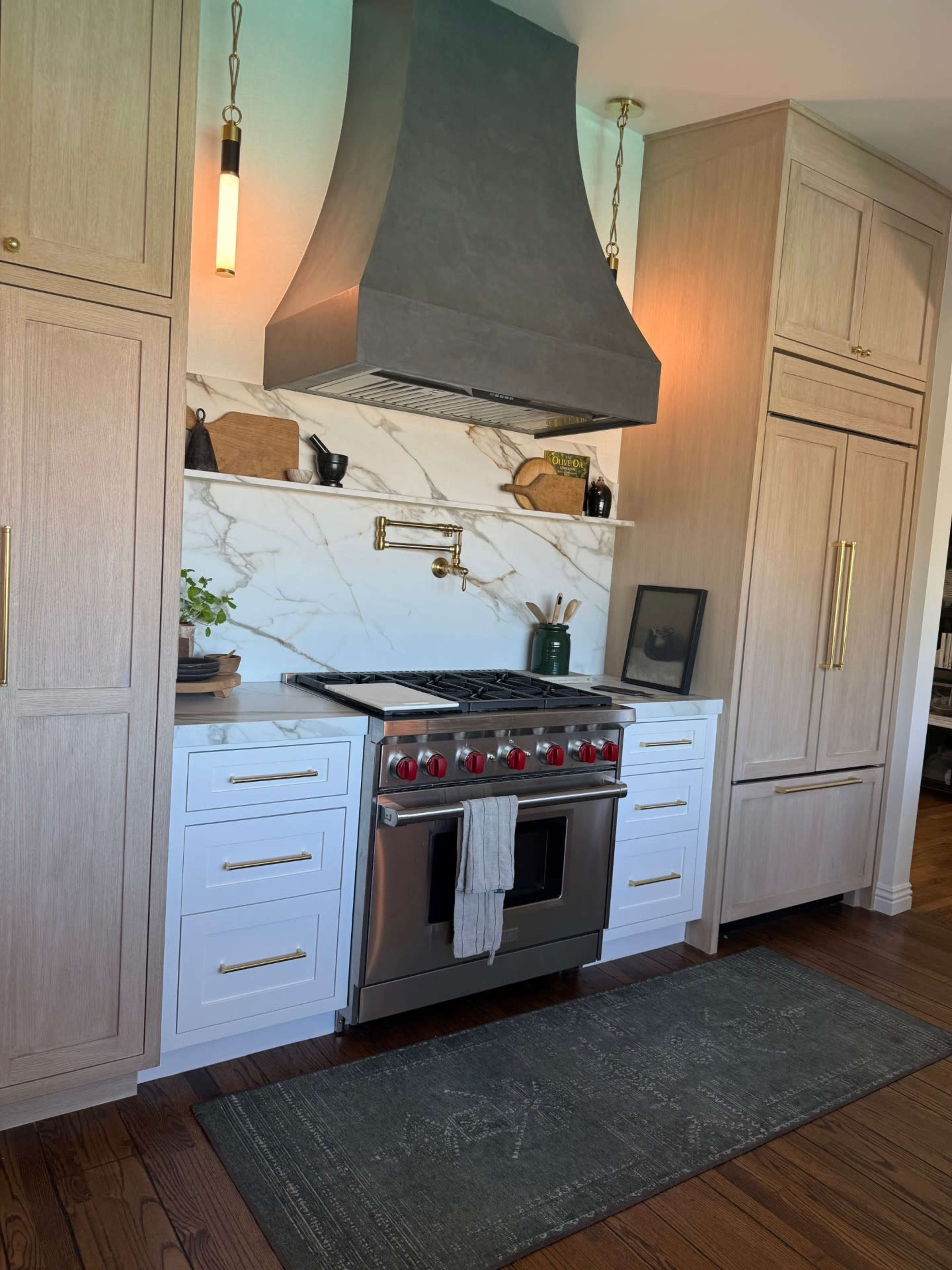 The image shows a modern kitchen with a marble backsplash, stainless steel range, and wooden cabinetry.