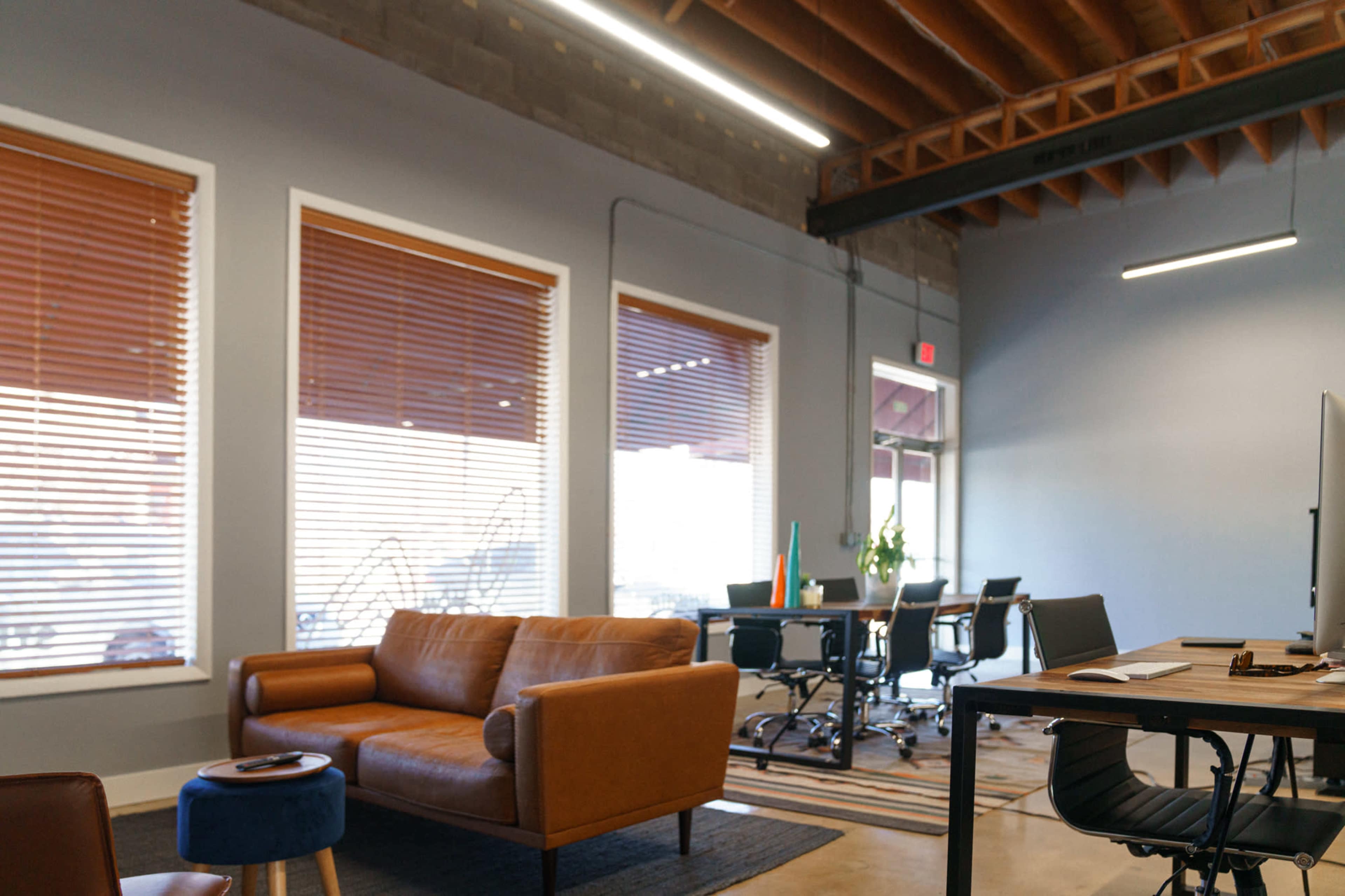 A modern office space with a brown leather sofa, a dark rug, and a workspace equipped with a desk and chairs.