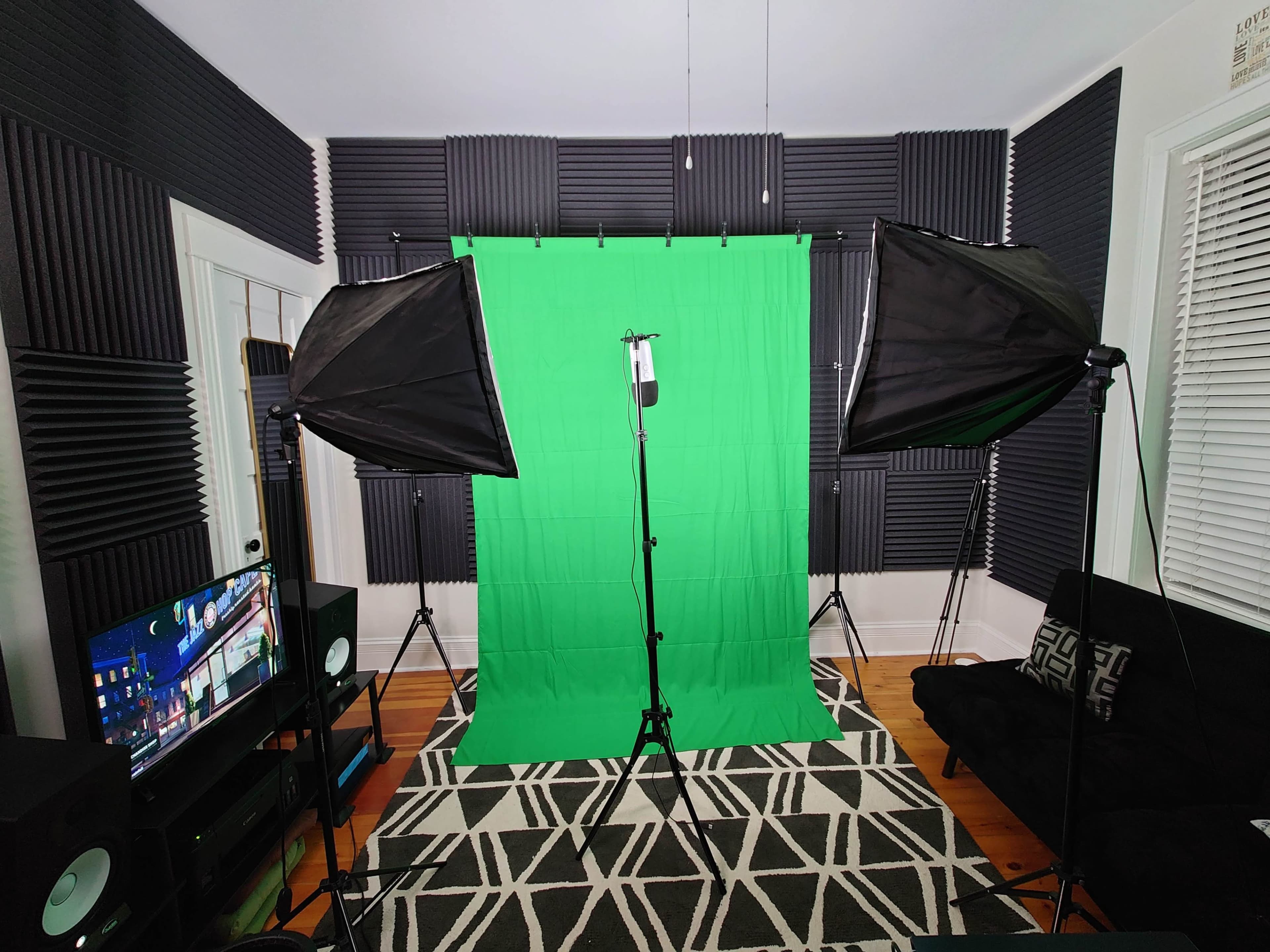 A photography studio setup features a green backdrop surrounded by softbox lights, with a television and a couch in the room.