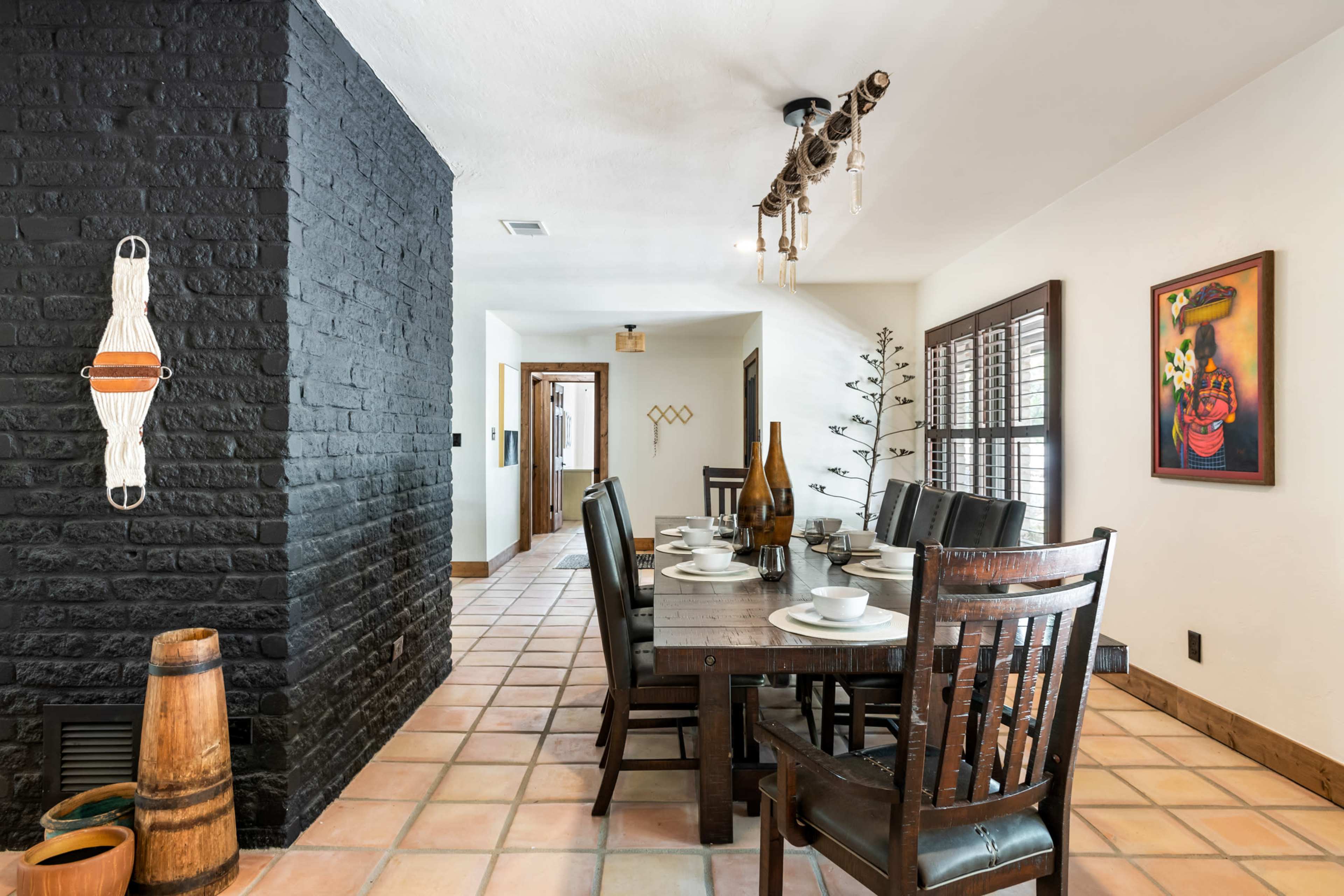 A dining area features a wooden table set for a meal, flanked by chairs, with a decorative black brick wall and a rustic light fixture overhead.