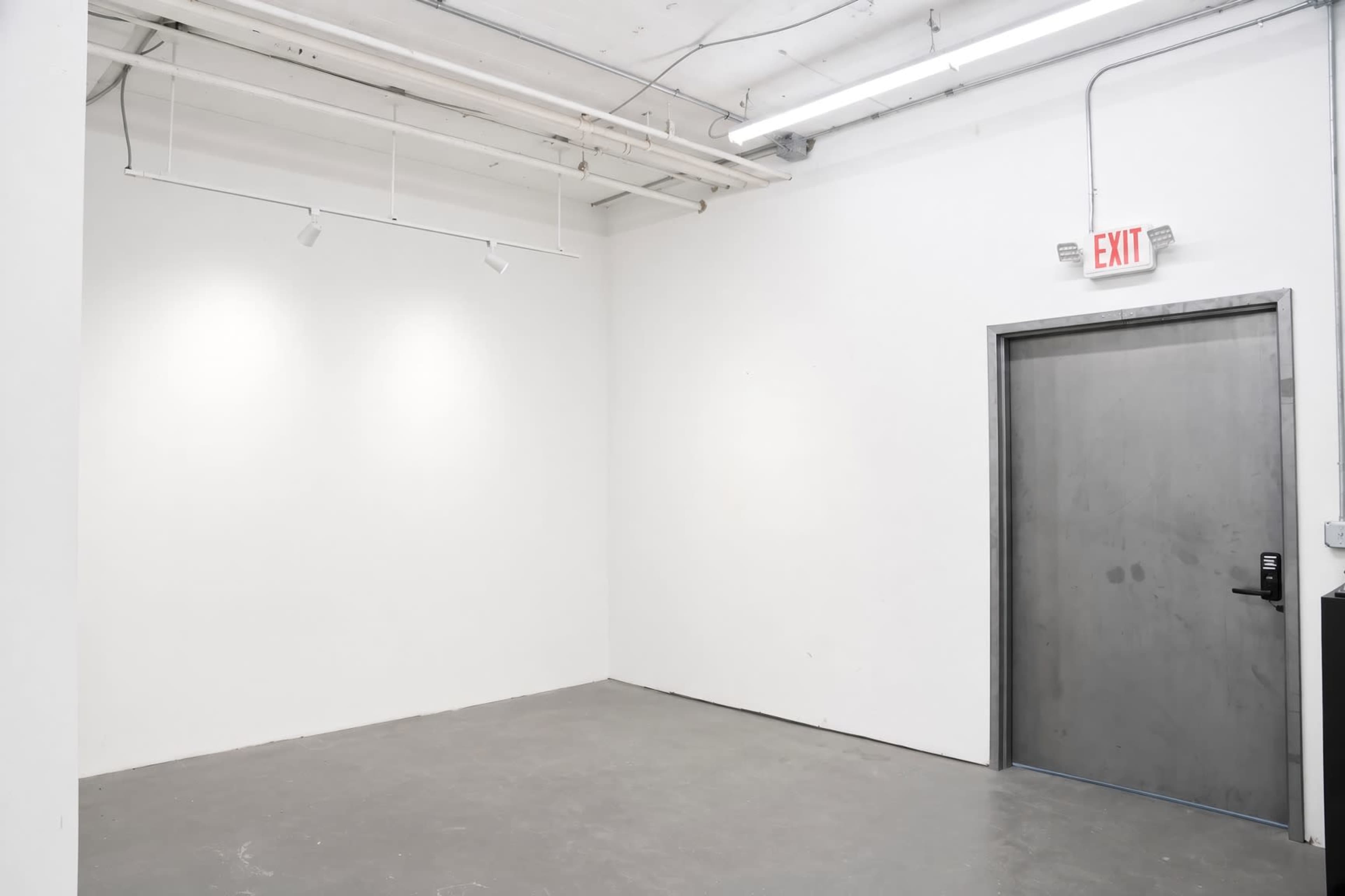 The image shows a bare room with white walls, a concrete floor, and an exit door on one side.