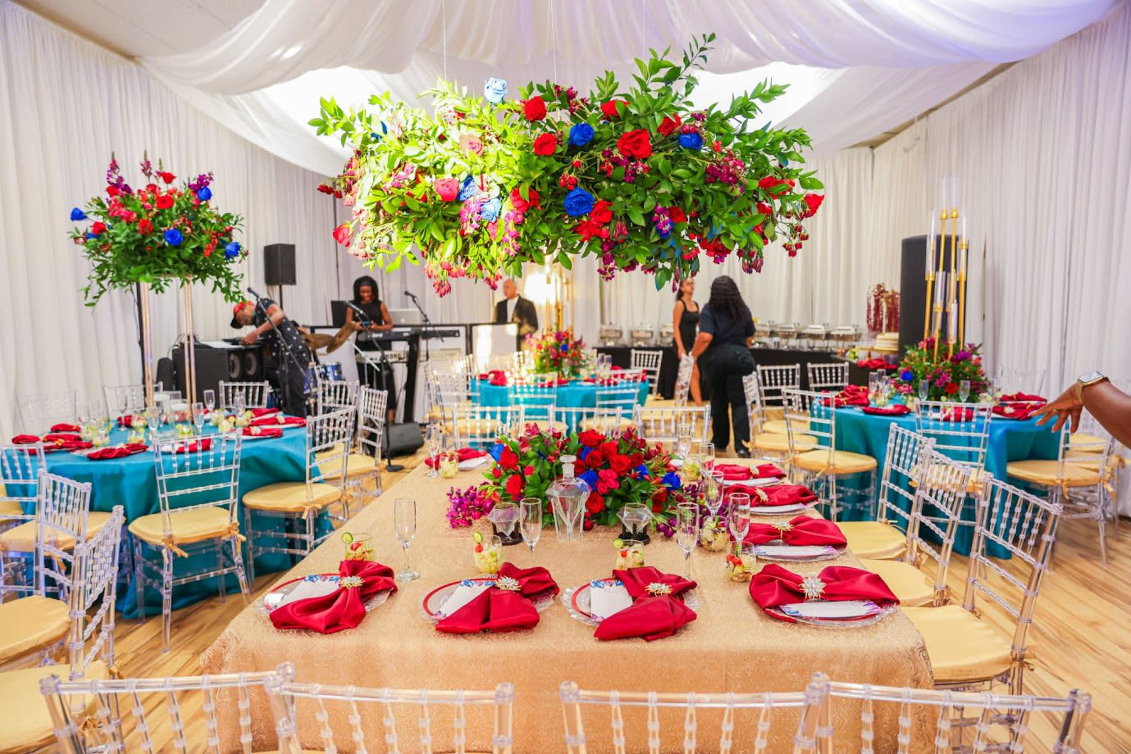 A decorated banquet hall features tables covered in bright colors, with large floral centerpieces and elegantly arranged place settings.