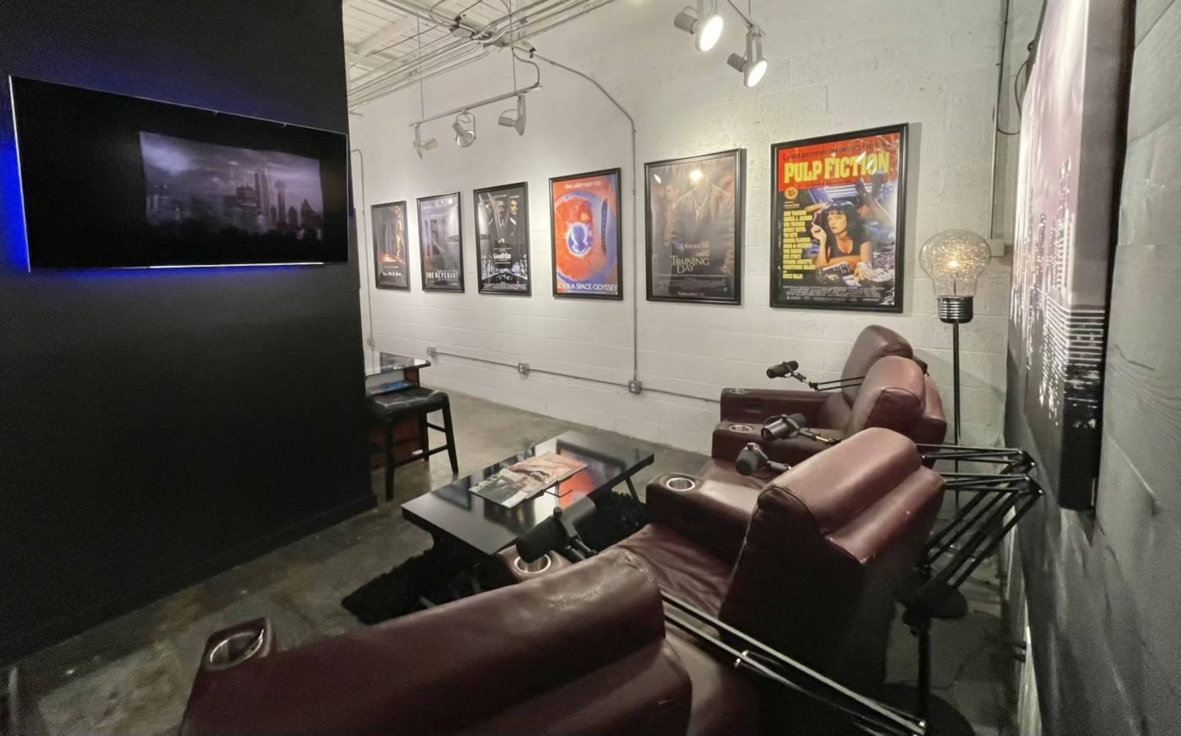 A small lounge area with brown recliner chairs, movie posters on the wall, and a low table featuring magazines and a lamp.