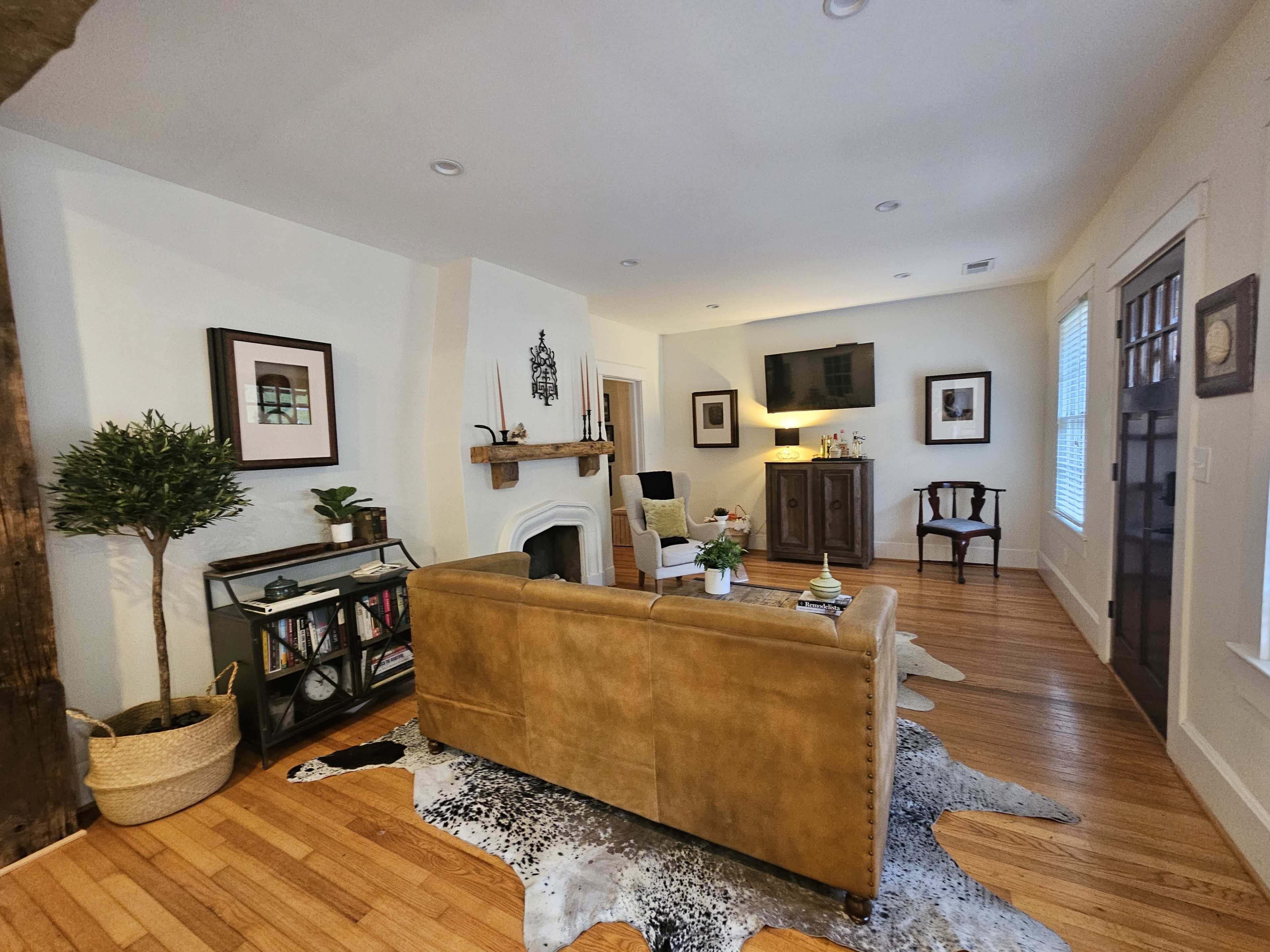 The image shows a cozy living room featuring a tan sofa, a wooden entertainment unit, and a coffee table on hardwood flooring.