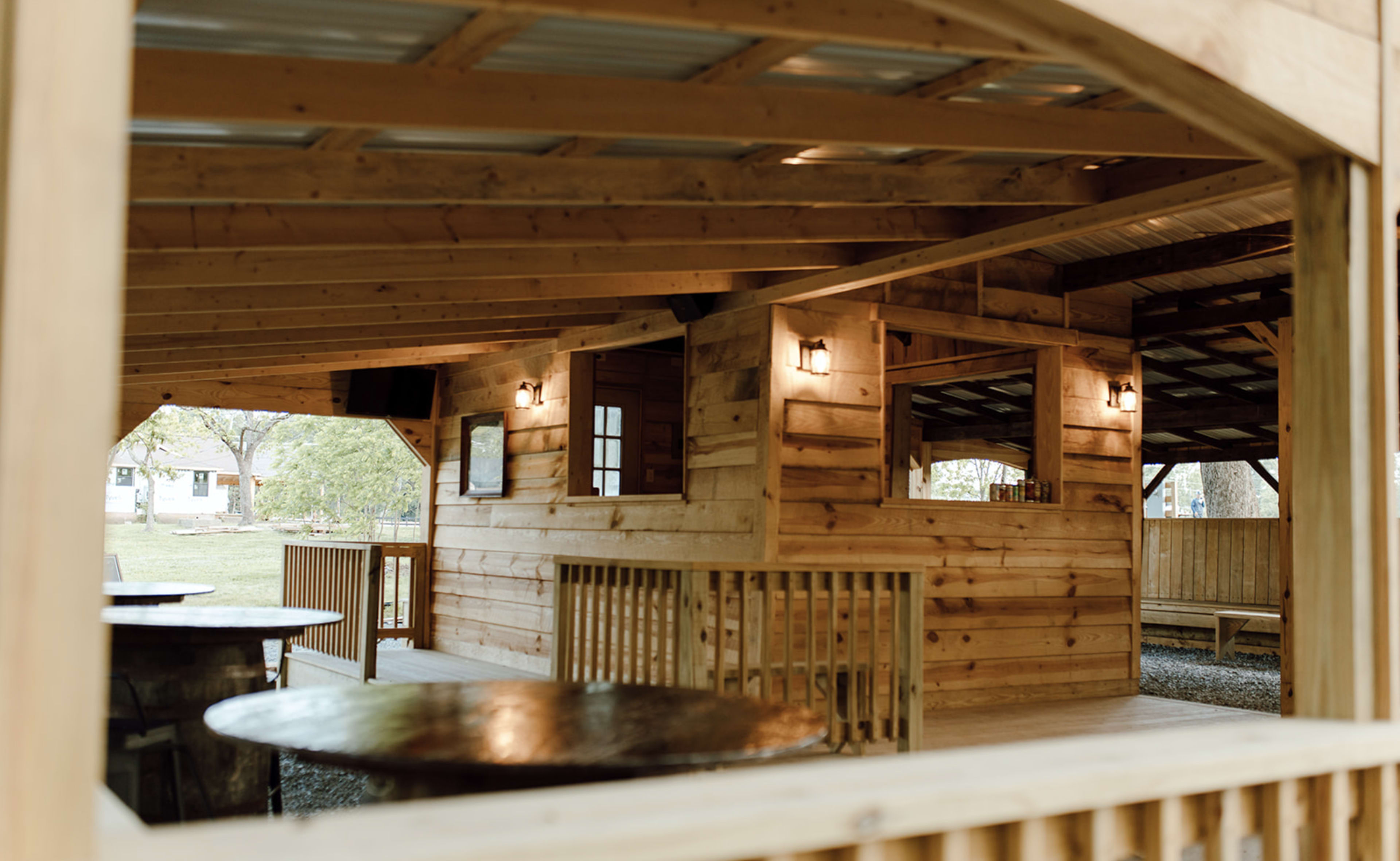 The image shows the interior of a wooden pavilion with exposed beams and tables.