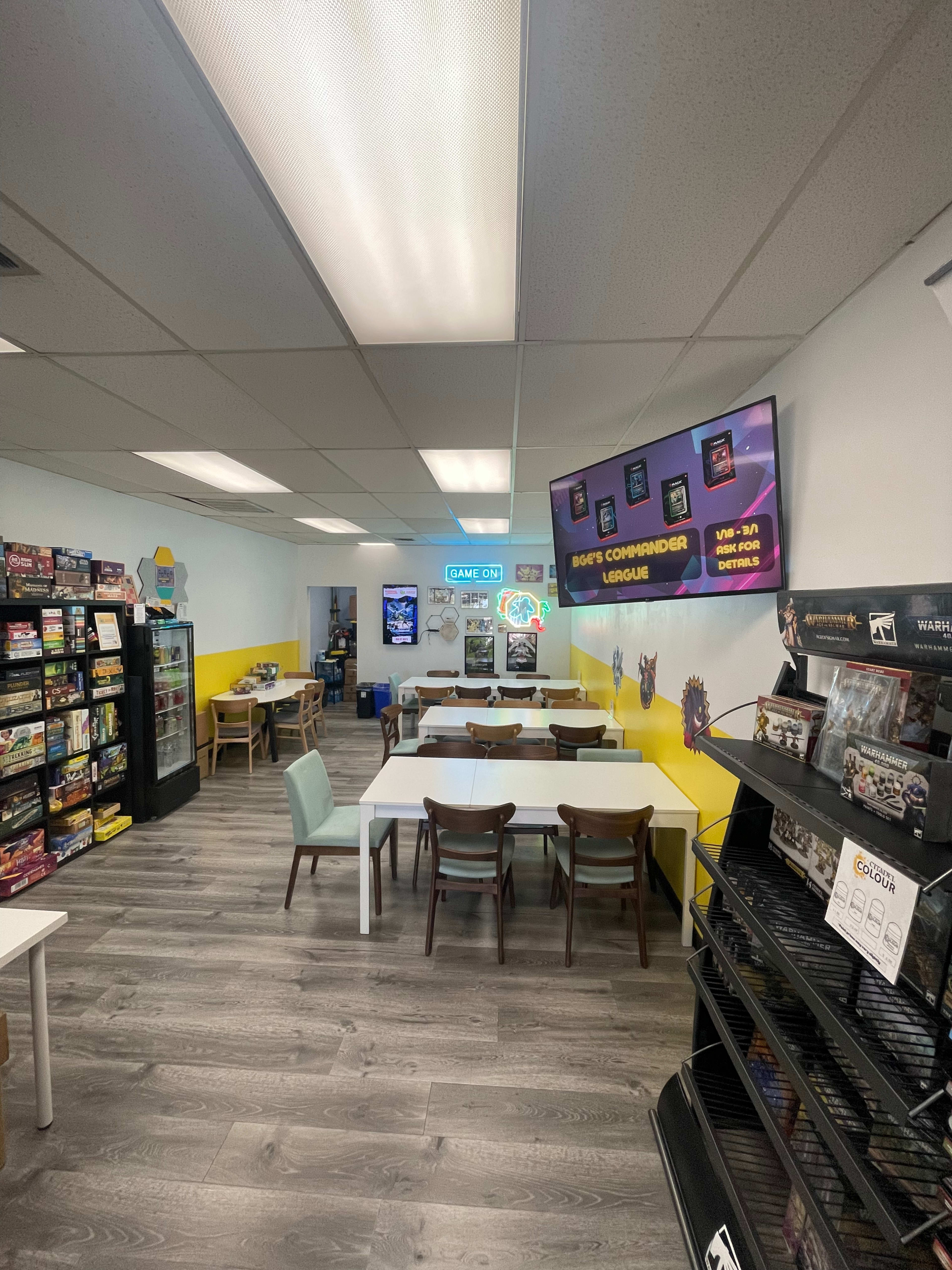 The interior of a brightly colored game store featuring tables for events, shelves of board games, and promotional displays on the walls.