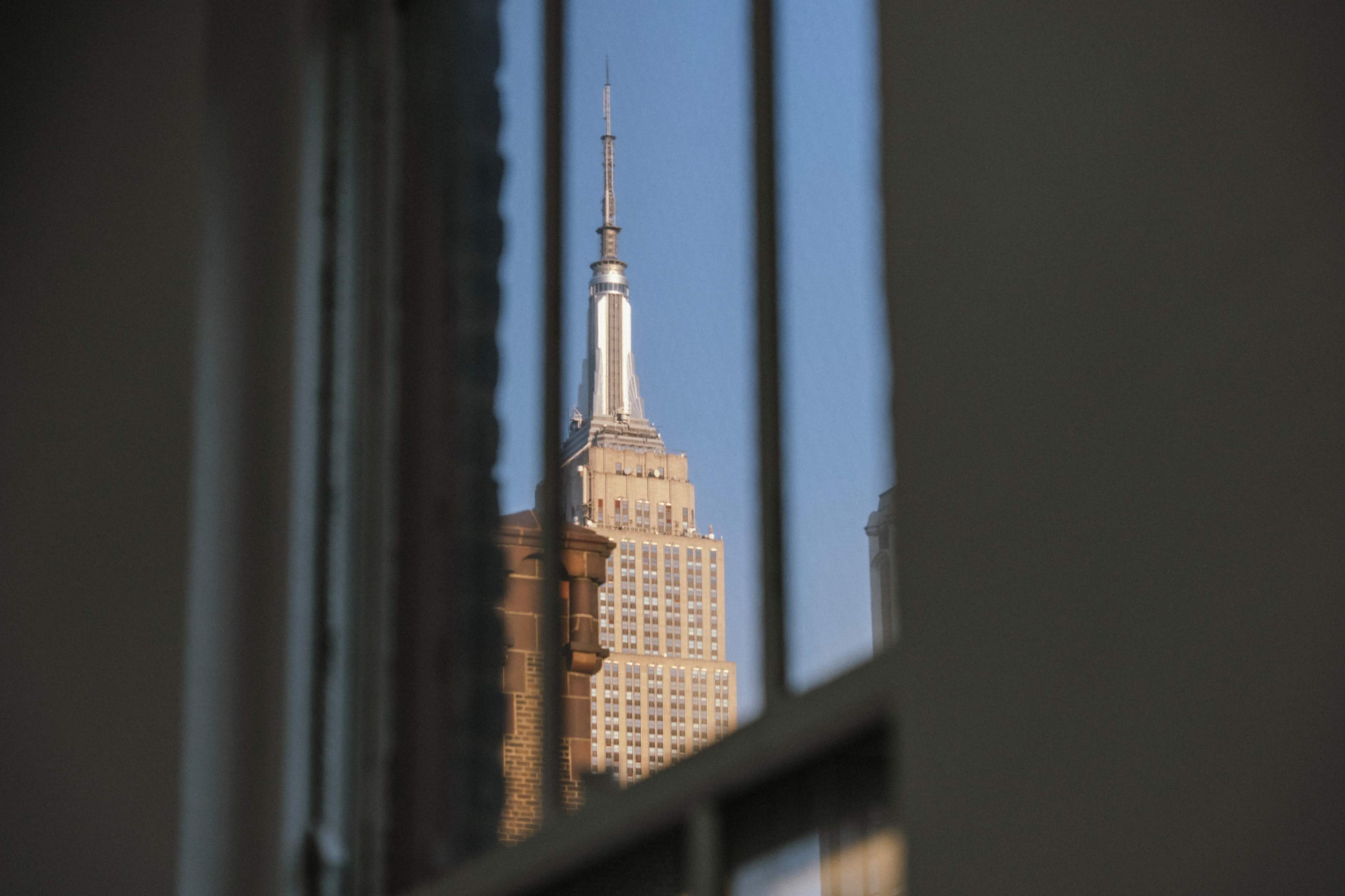 The Empire State Building is visible through a window reflection against a clear blue sky.
