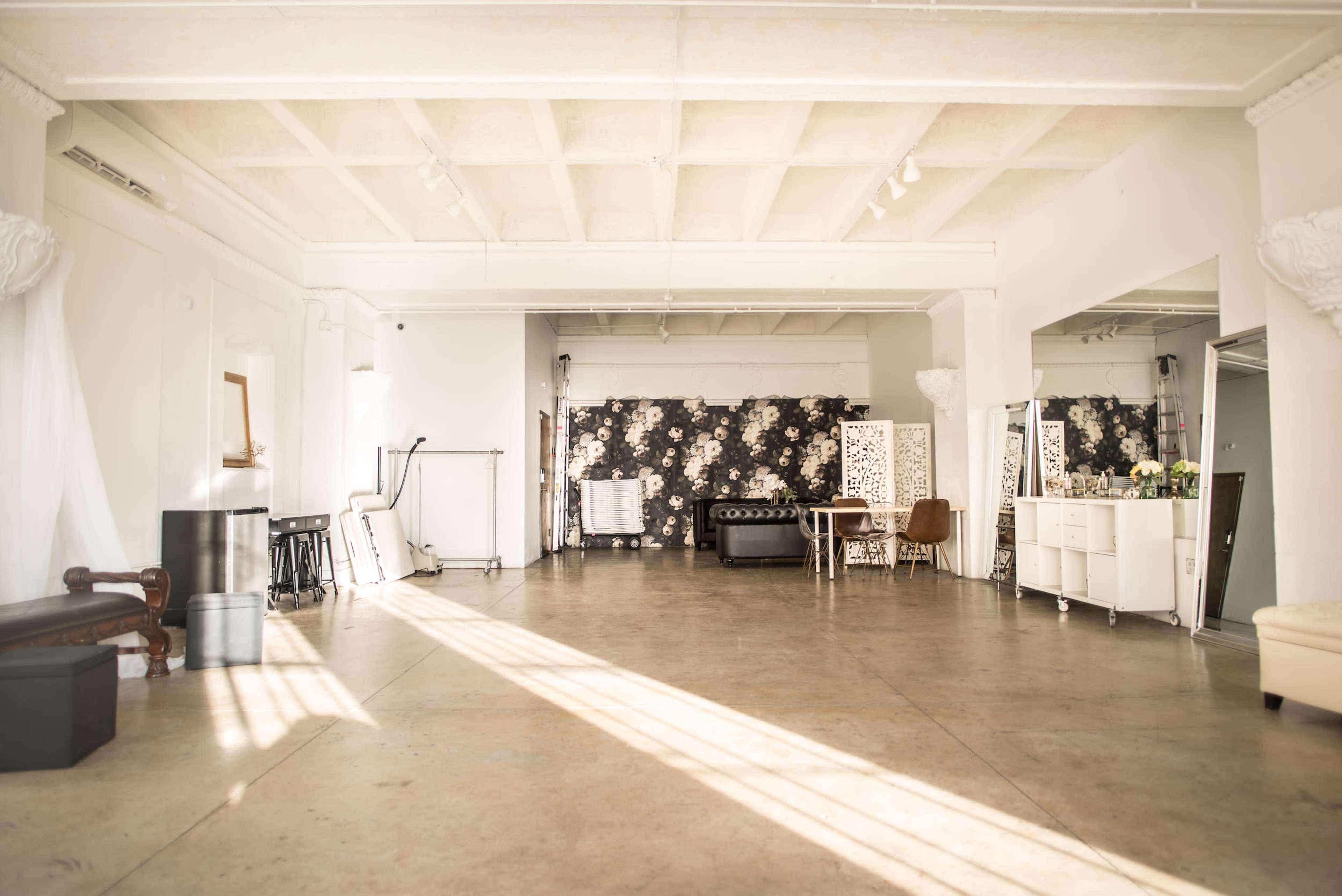 A spacious, well-lit interior featuring a floral wallpaper backdrop, a decorative couch, and various pieces of furniture arranged in an open area.