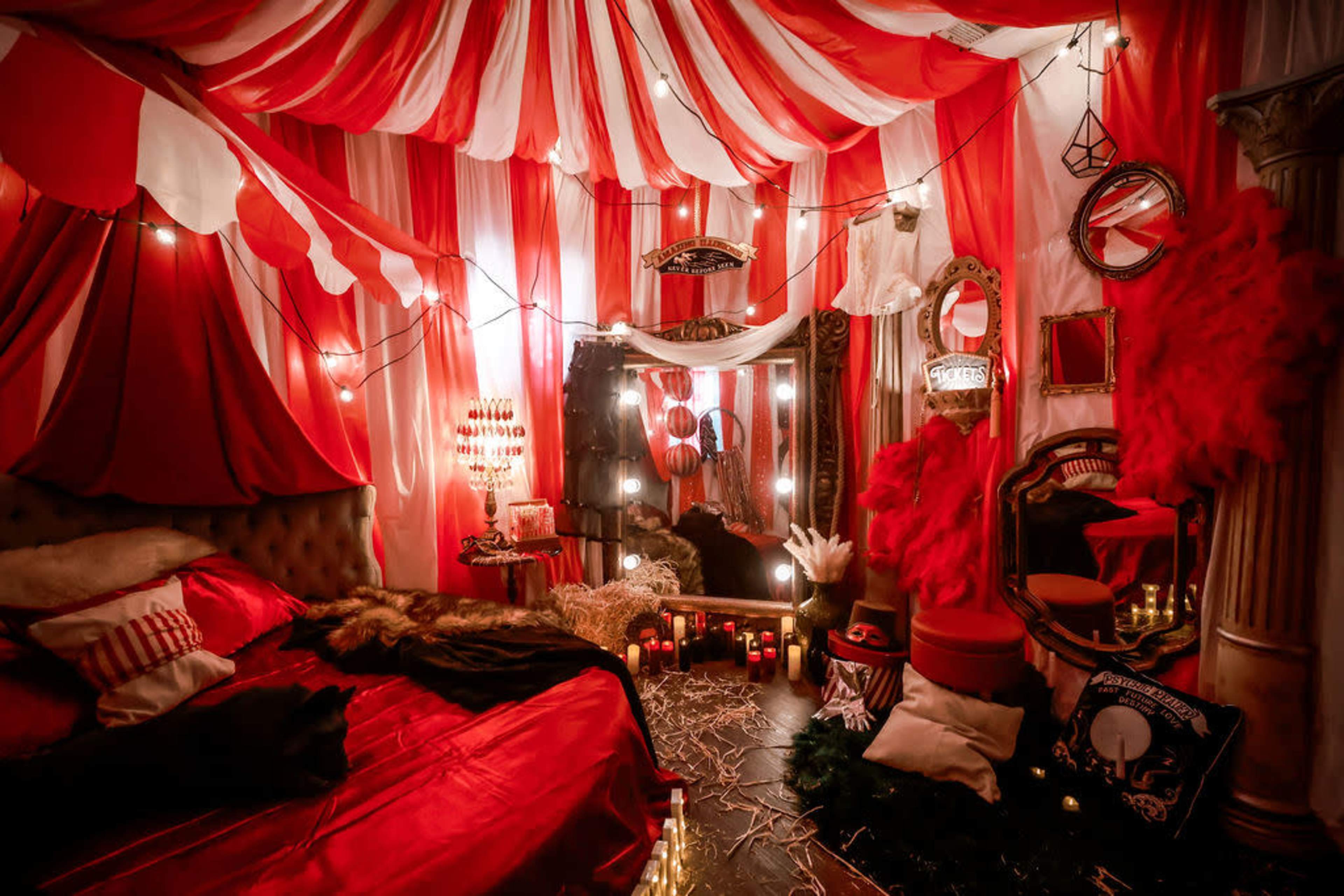 The image shows a decorative bedroom with red and white striped fabric draping the ceiling, soft lighting, and various themed decor elements, including candles and mirrors.
