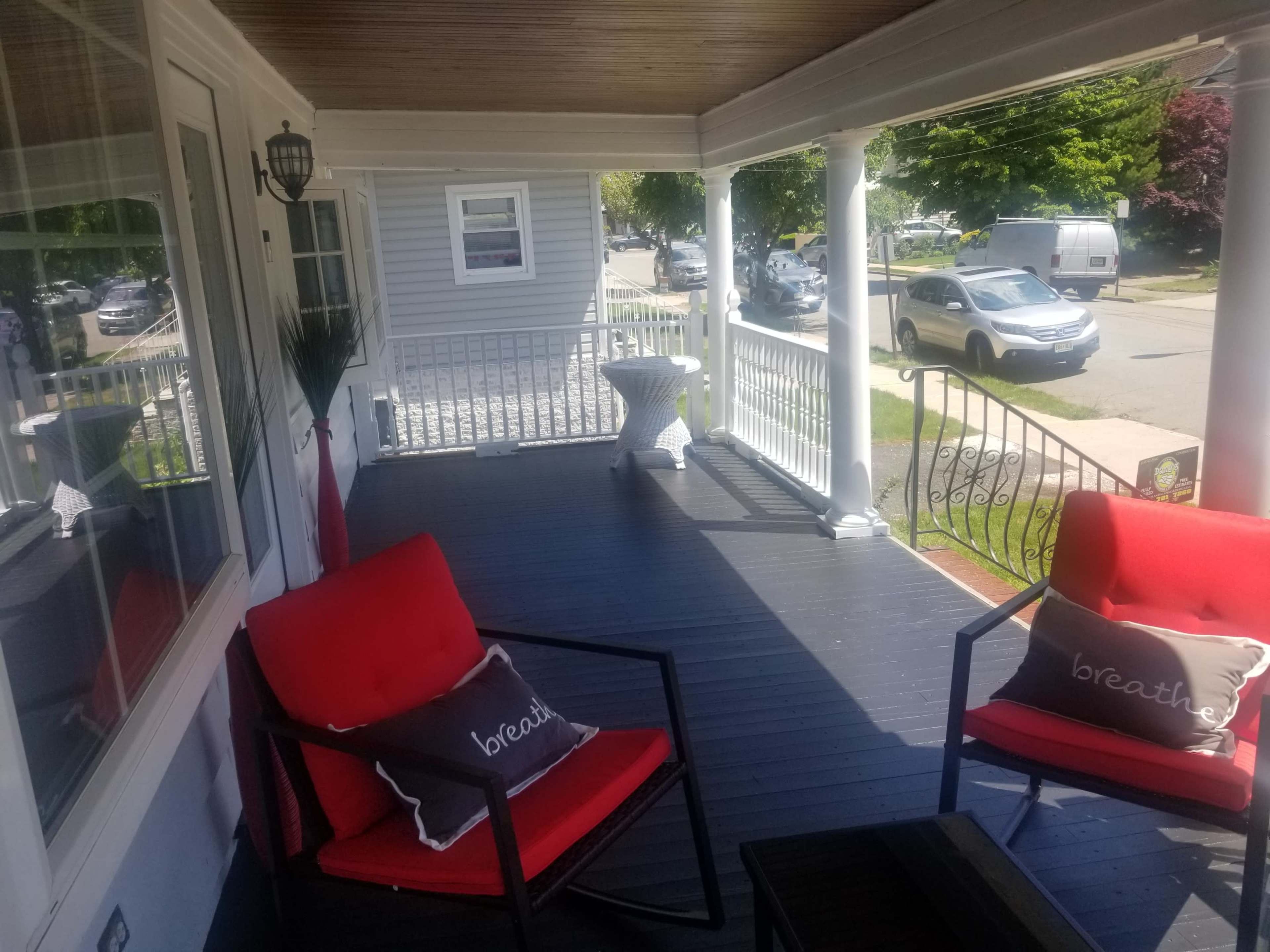 A porch with two red chairs positioned beside a small table, overlooking a street lined with parked cars.
