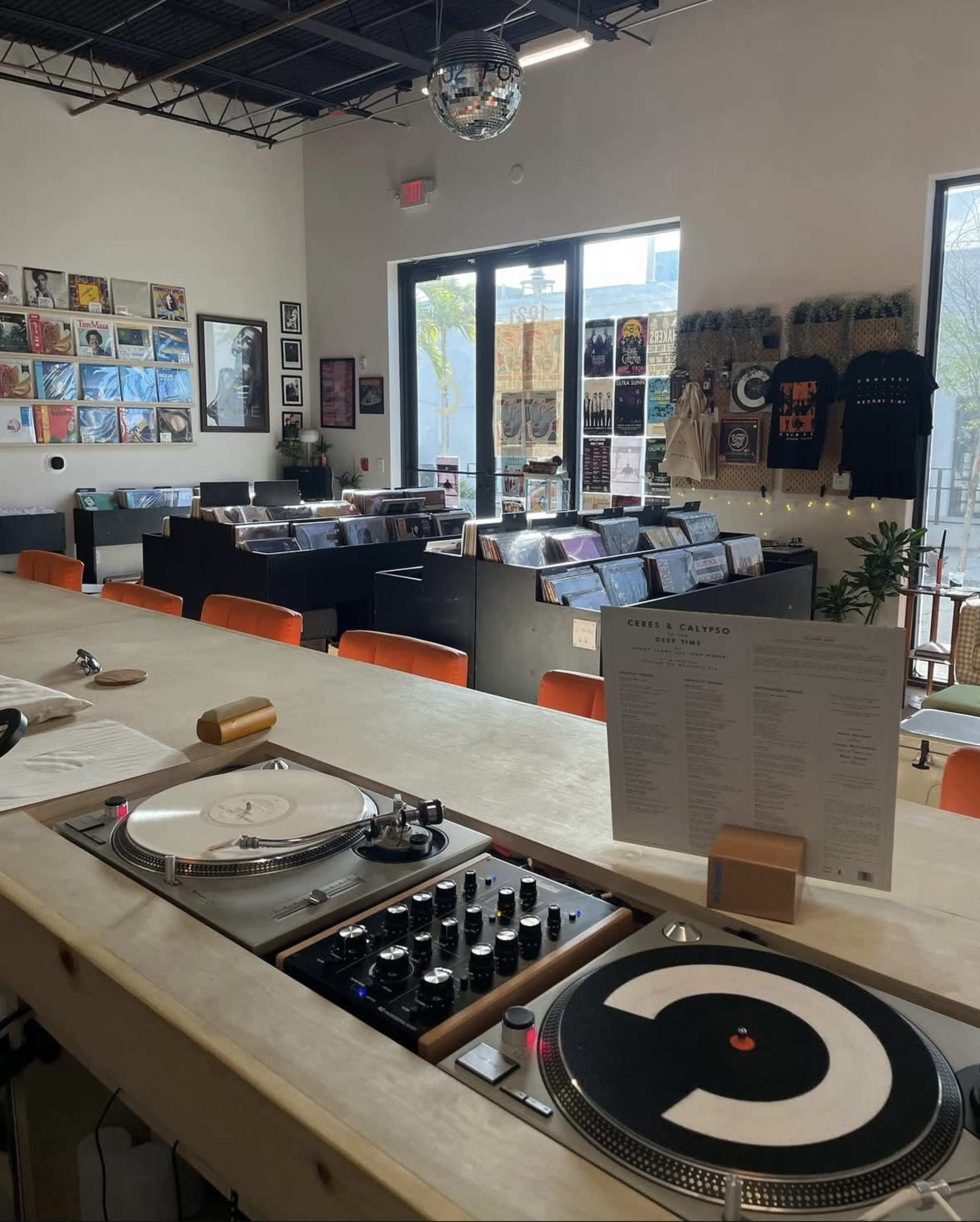 The image shows a record store with a bar area featuring turntables, a menu, and shelves filled with vinyl records in the background.