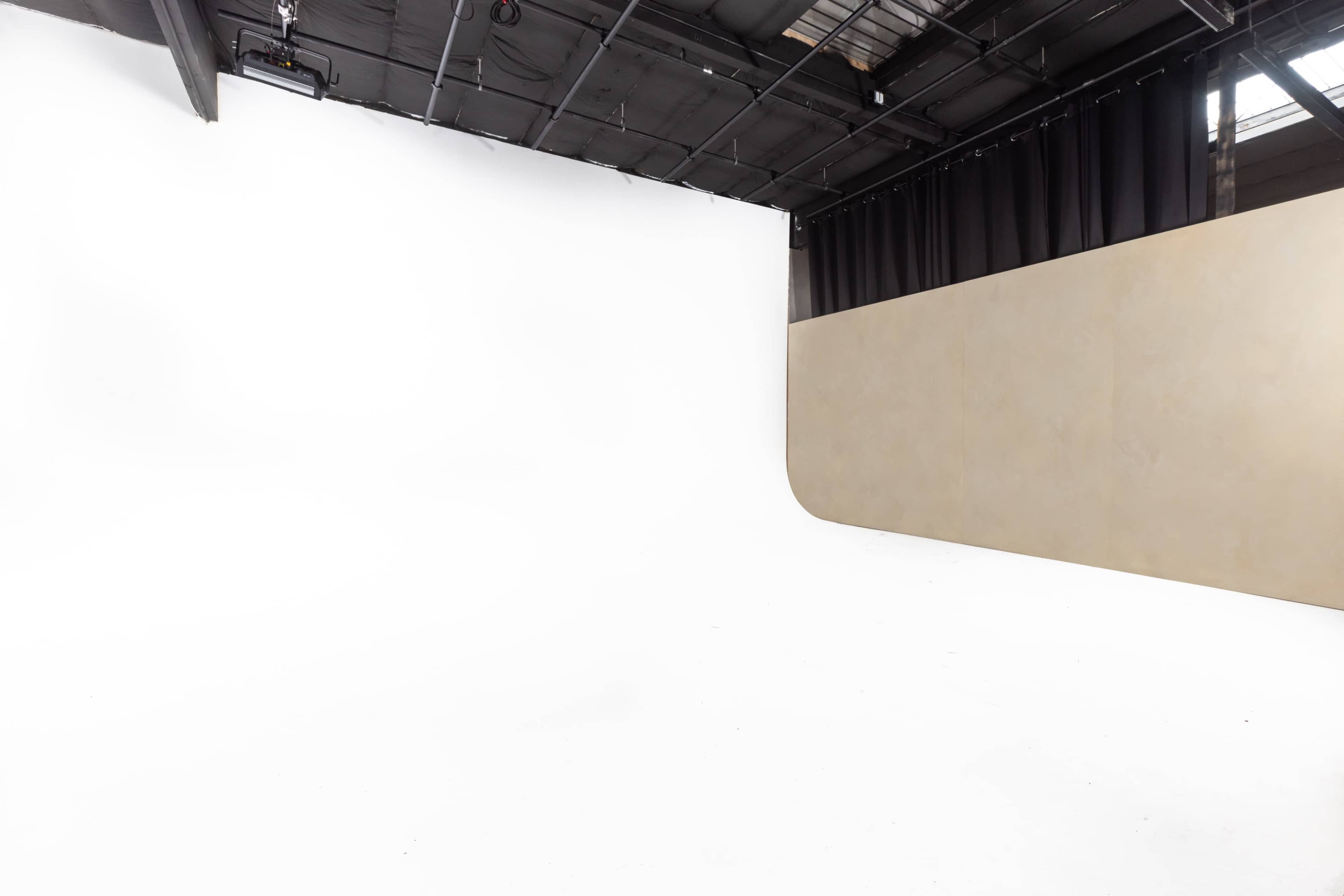 The image shows a spacious photography studio with a seamless white backdrop on one side and a curved beige backdrop on the other.