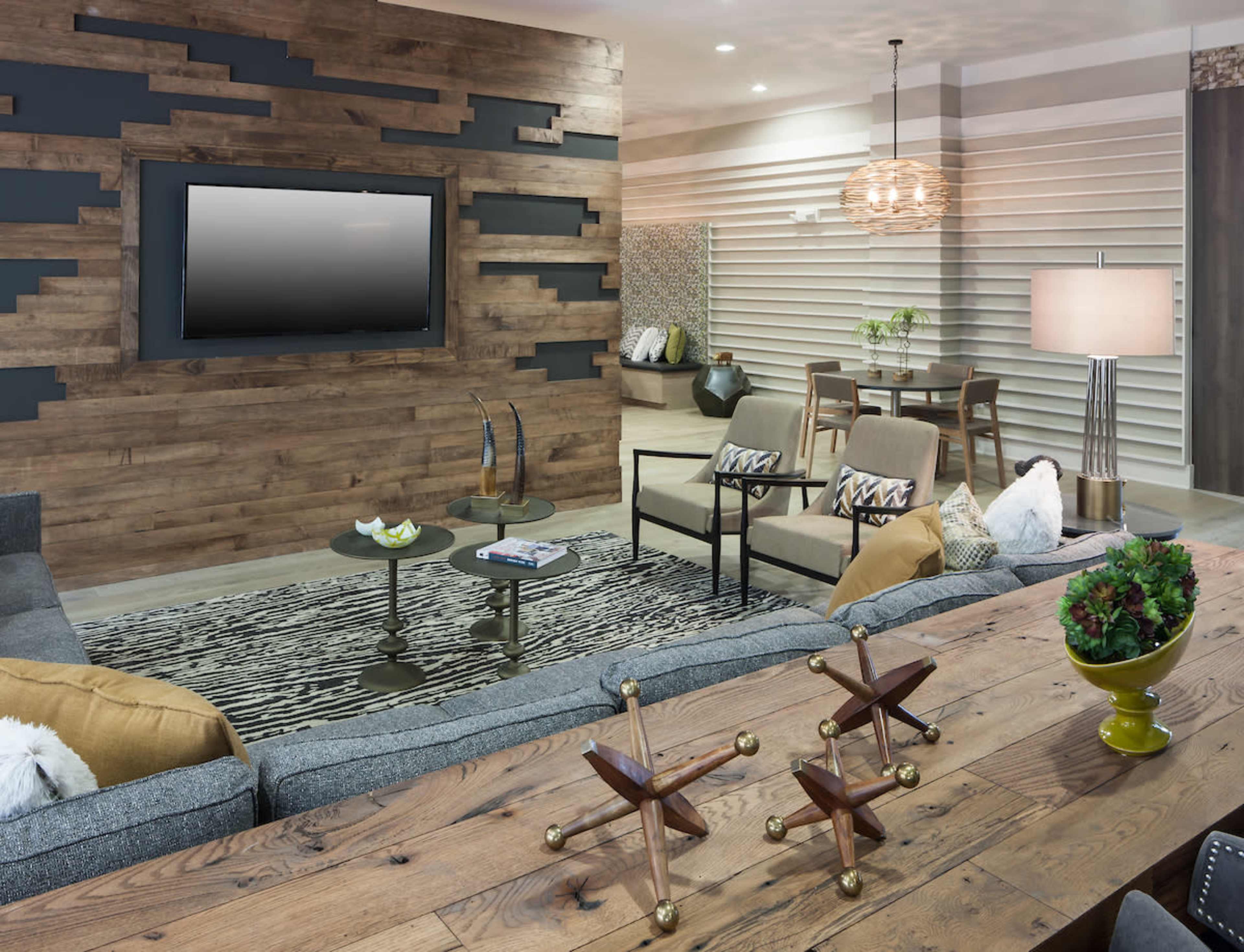 A modern living room features a textured wood-paneled wall, a large gray sectional sofa, and stylish furniture arranged around a central coffee table.