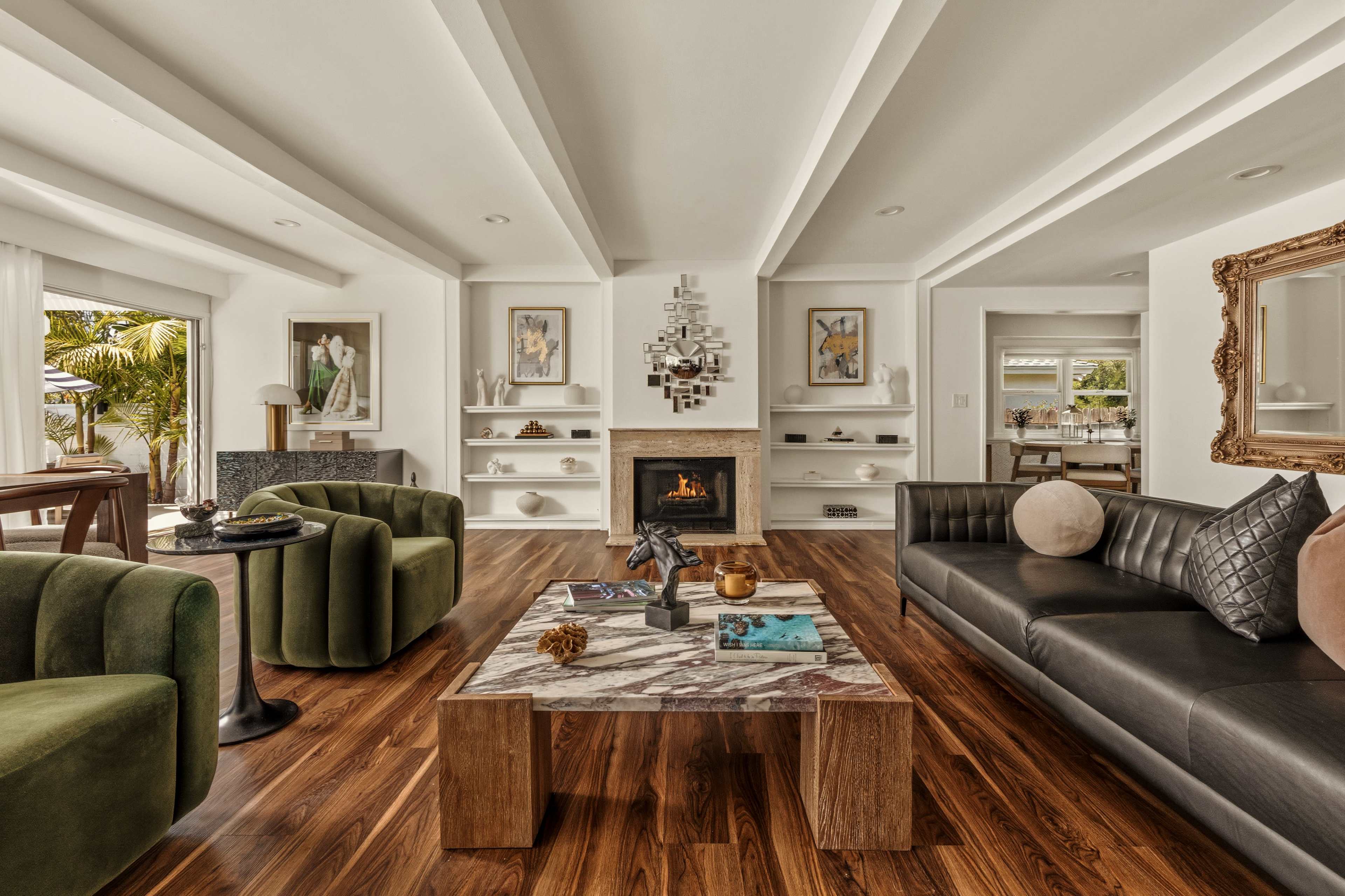 The living room features a modern design with a fireplace at the center, surrounded by plush seating, a large coffee table, and decorative artwork on the walls.