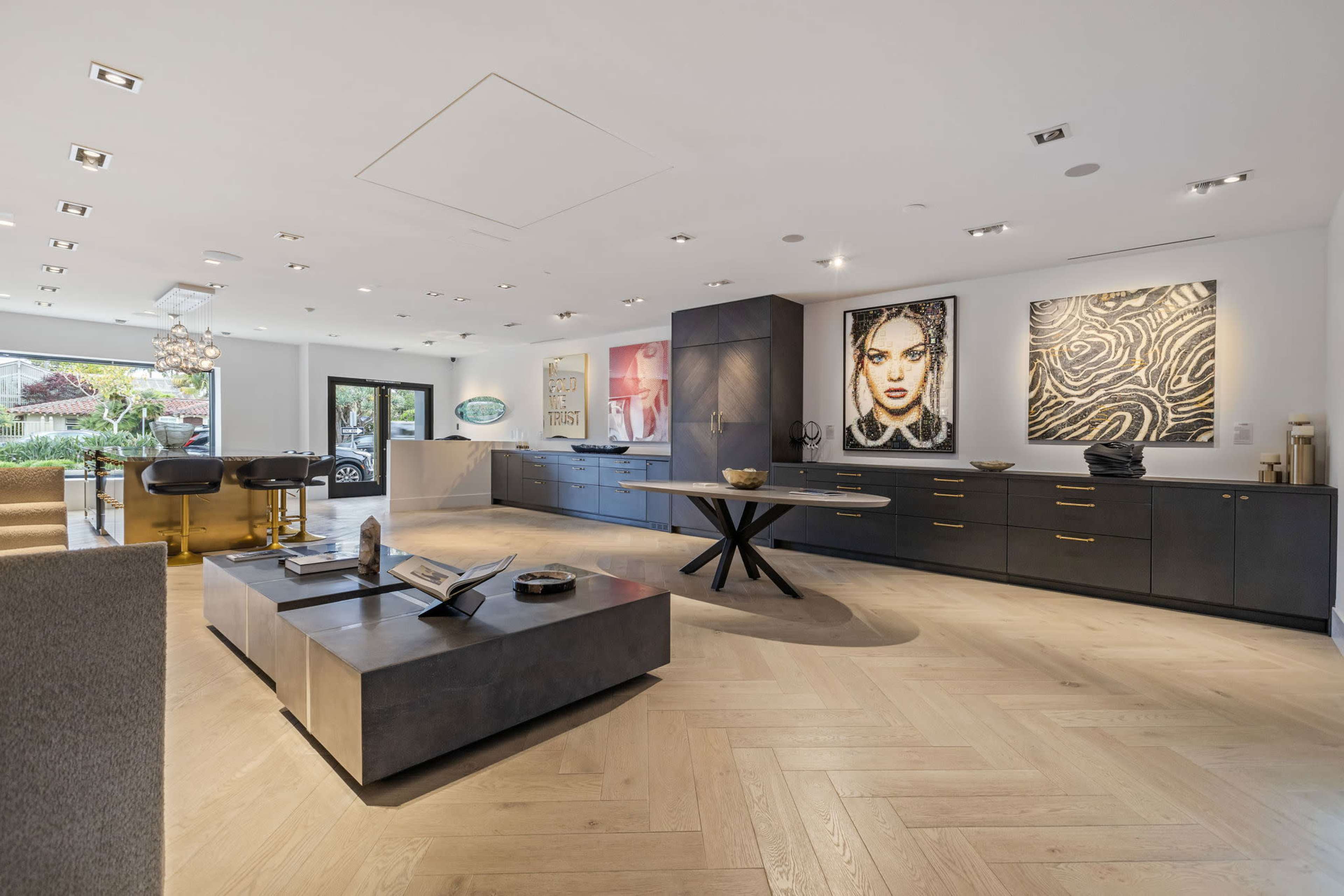 The interior of a modern art gallery features a sleek kitchen area and large artwork on display, with wood flooring and a central dining table.