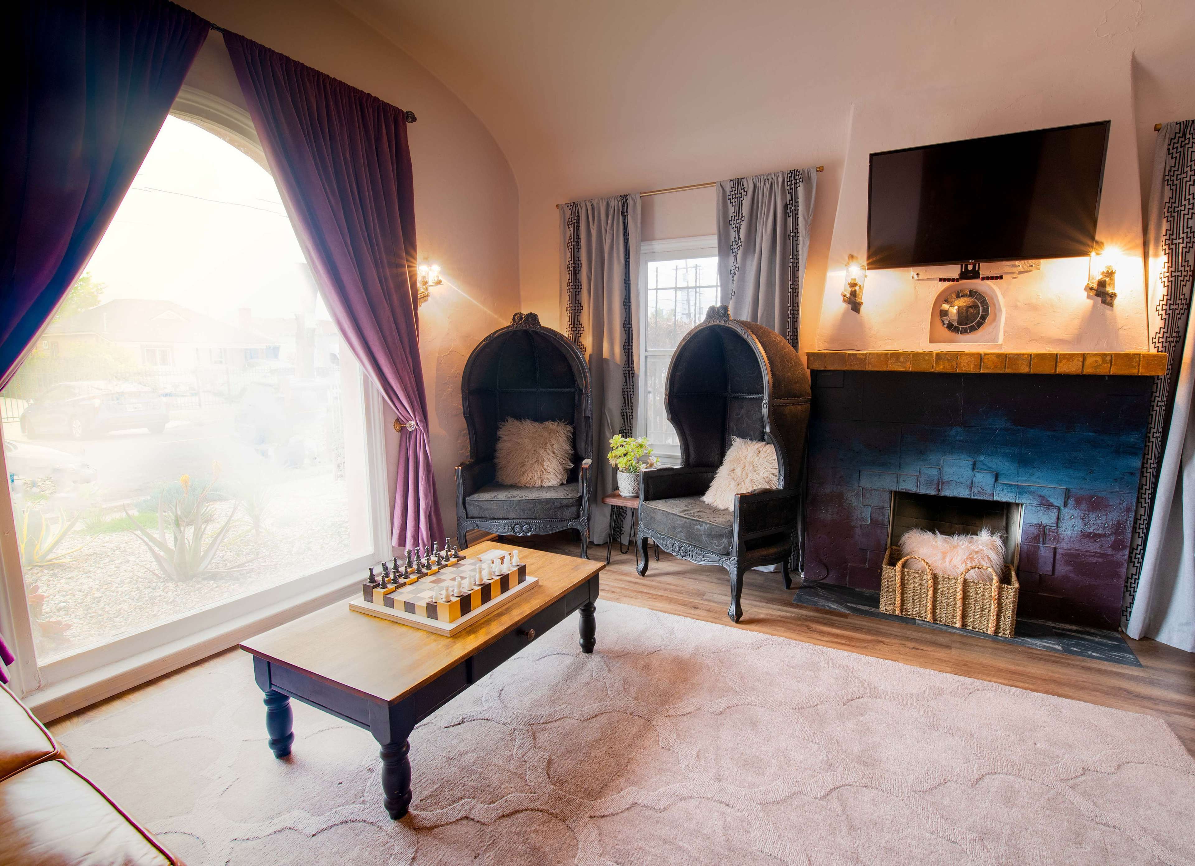 The room features two black upholstered chairs beside a fireplace, with a wooden coffee table in the center and large windows letting in natural light.