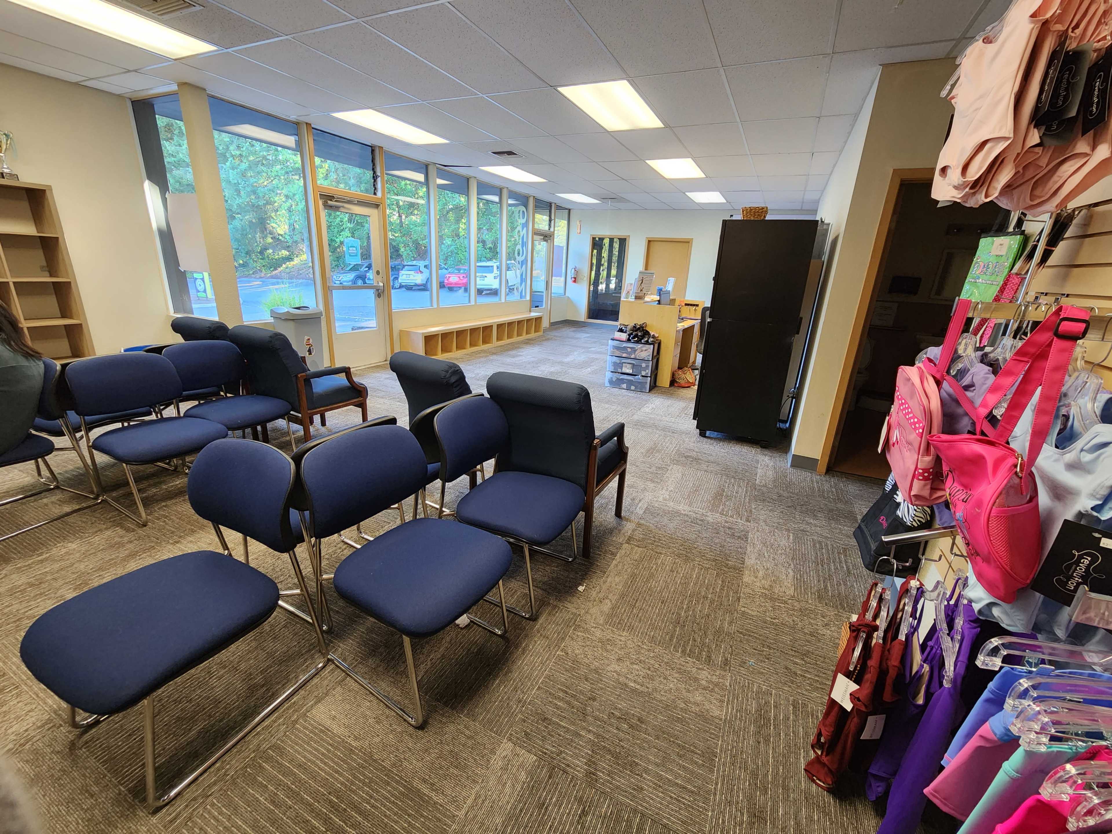 A waiting area with blue chairs arranged in rows, a reception desk, and shelves displaying various items.