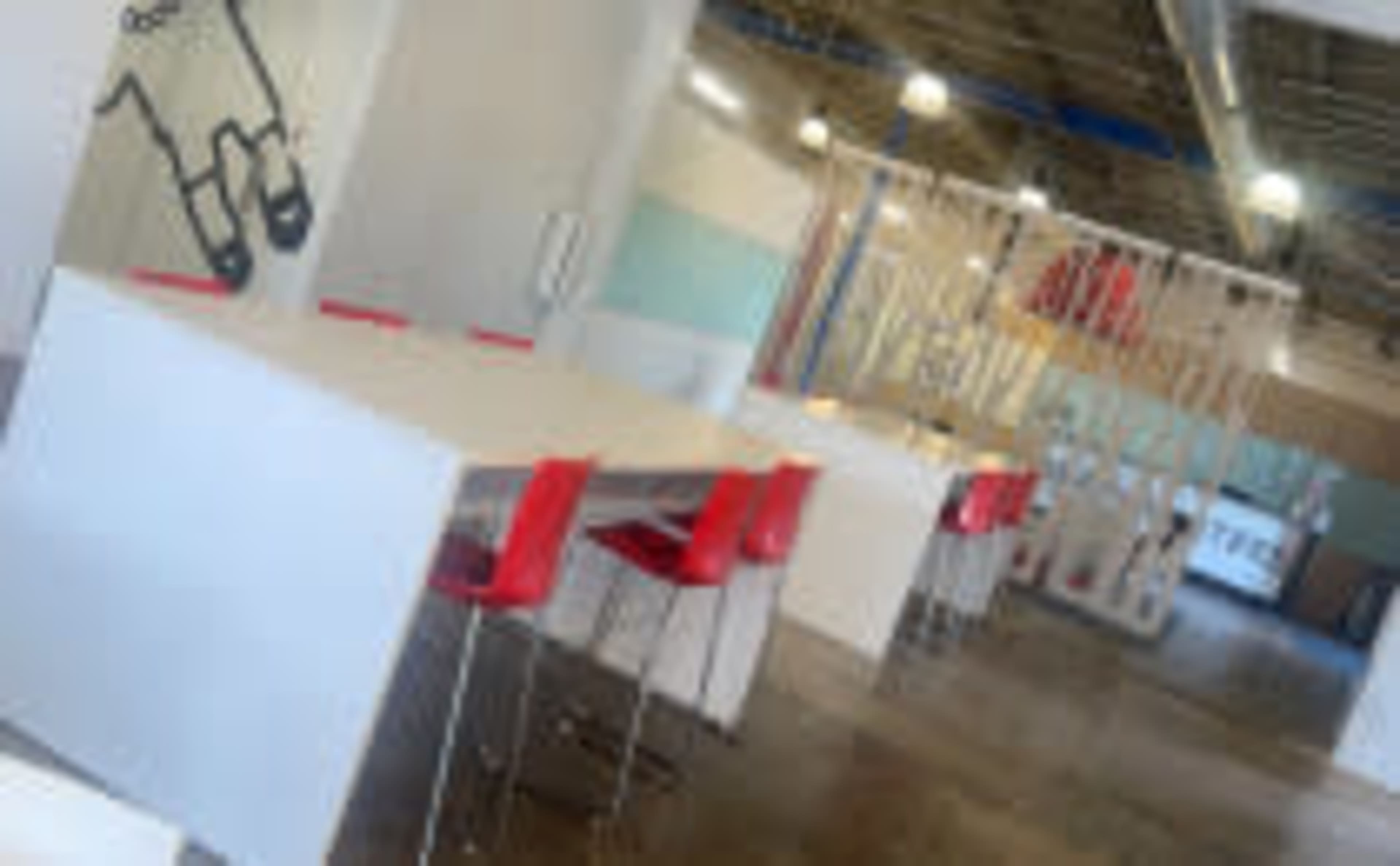 A modern workspace featuring several white tables paired with red chairs in a brightly lit, open environment.