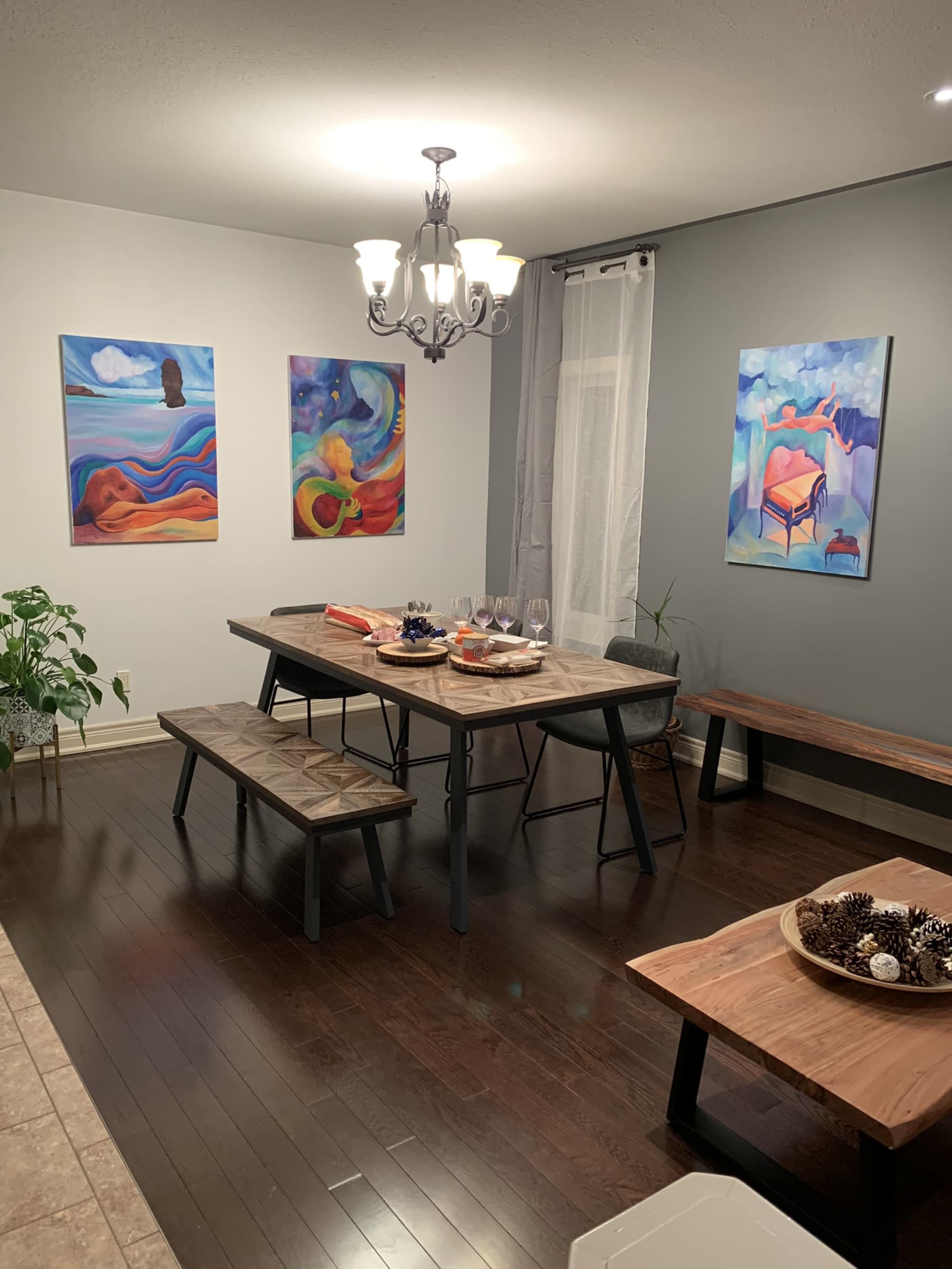 A dining room features a wooden table with benches surrounded by colorful abstract artwork on the walls.