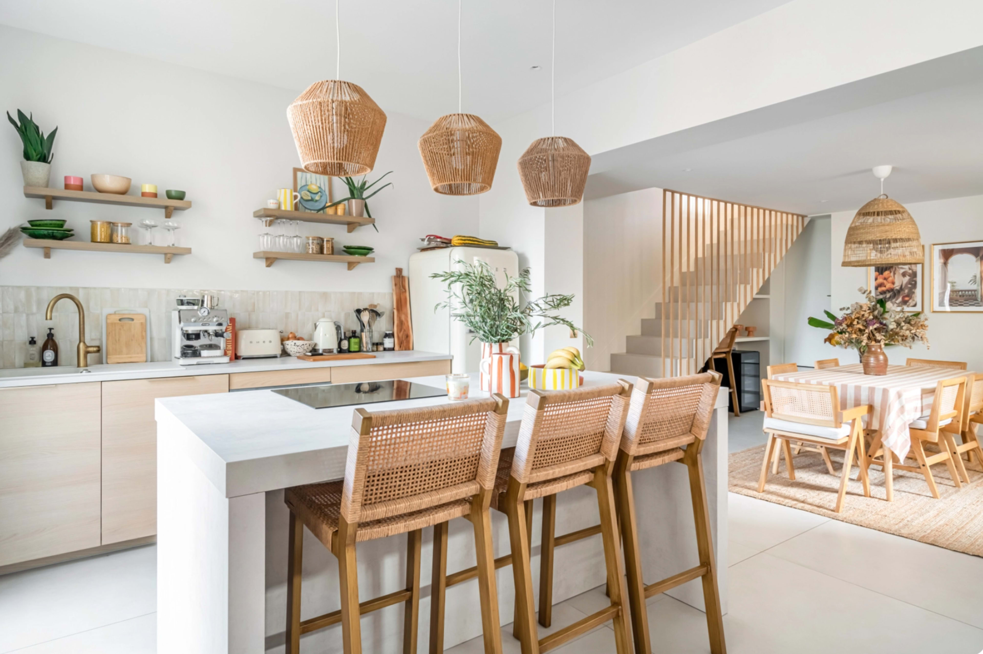 A modern kitchen features a central island with seating, natural wood accents, and a dining area in the background.