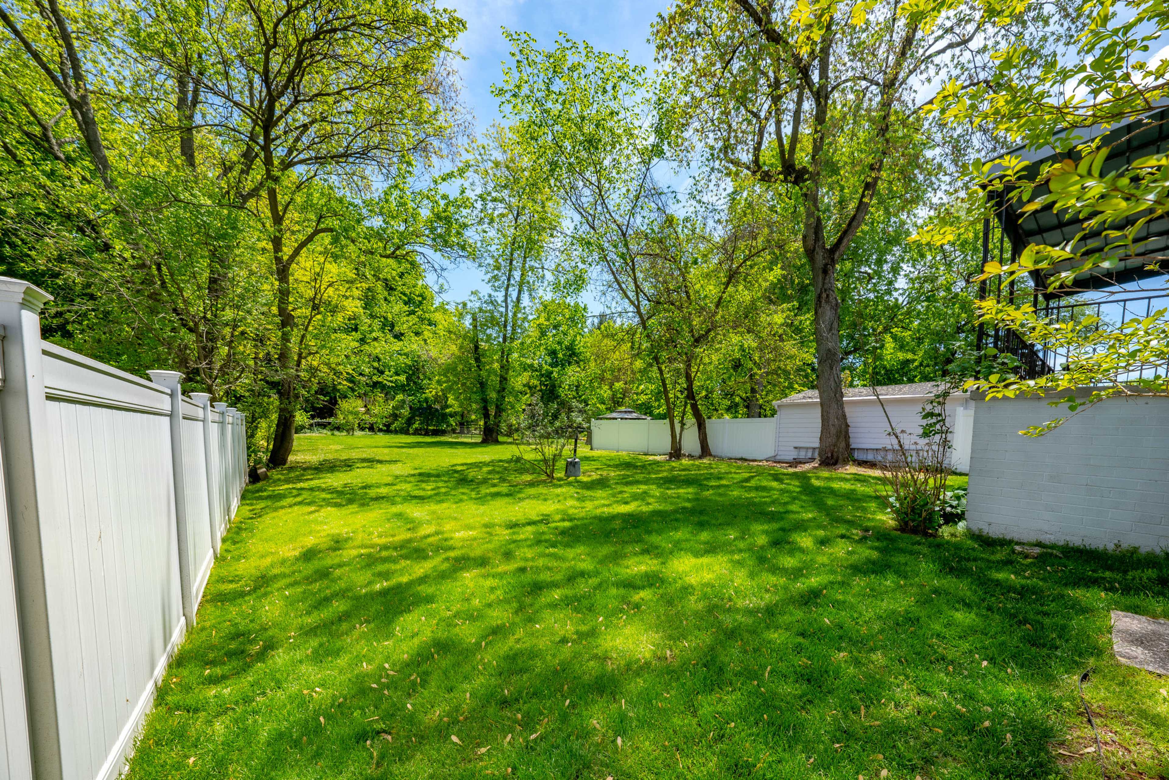 The image shows a spacious green lawn surrounded by trees and a white fence on one side.