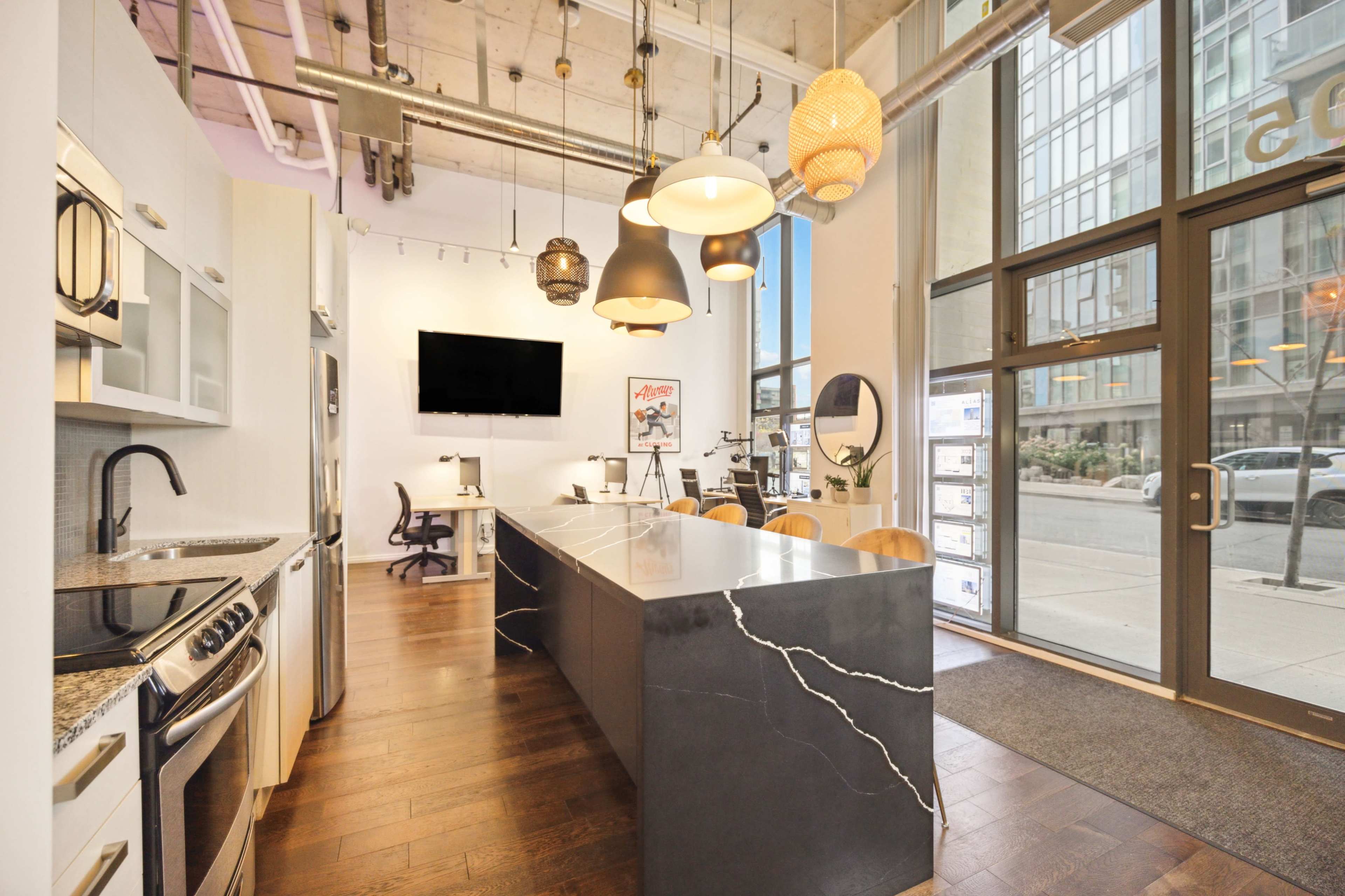 The image shows a modern kitchen with a large island, stainless steel appliances, and a seating area, set in a well-lit open space with large windows.