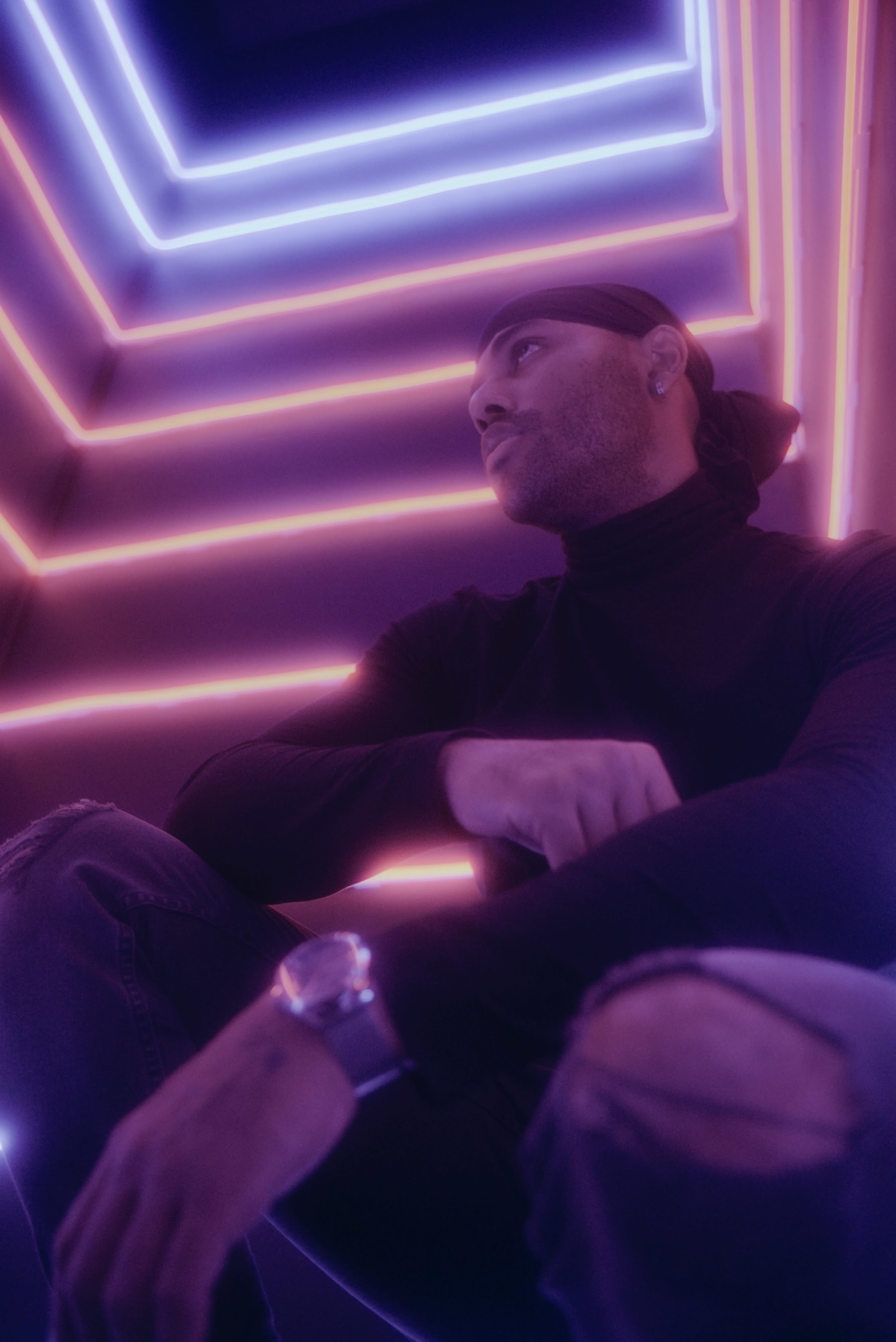A man sits in a dimly lit space with purple and pink neon lights illuminating the walls.
