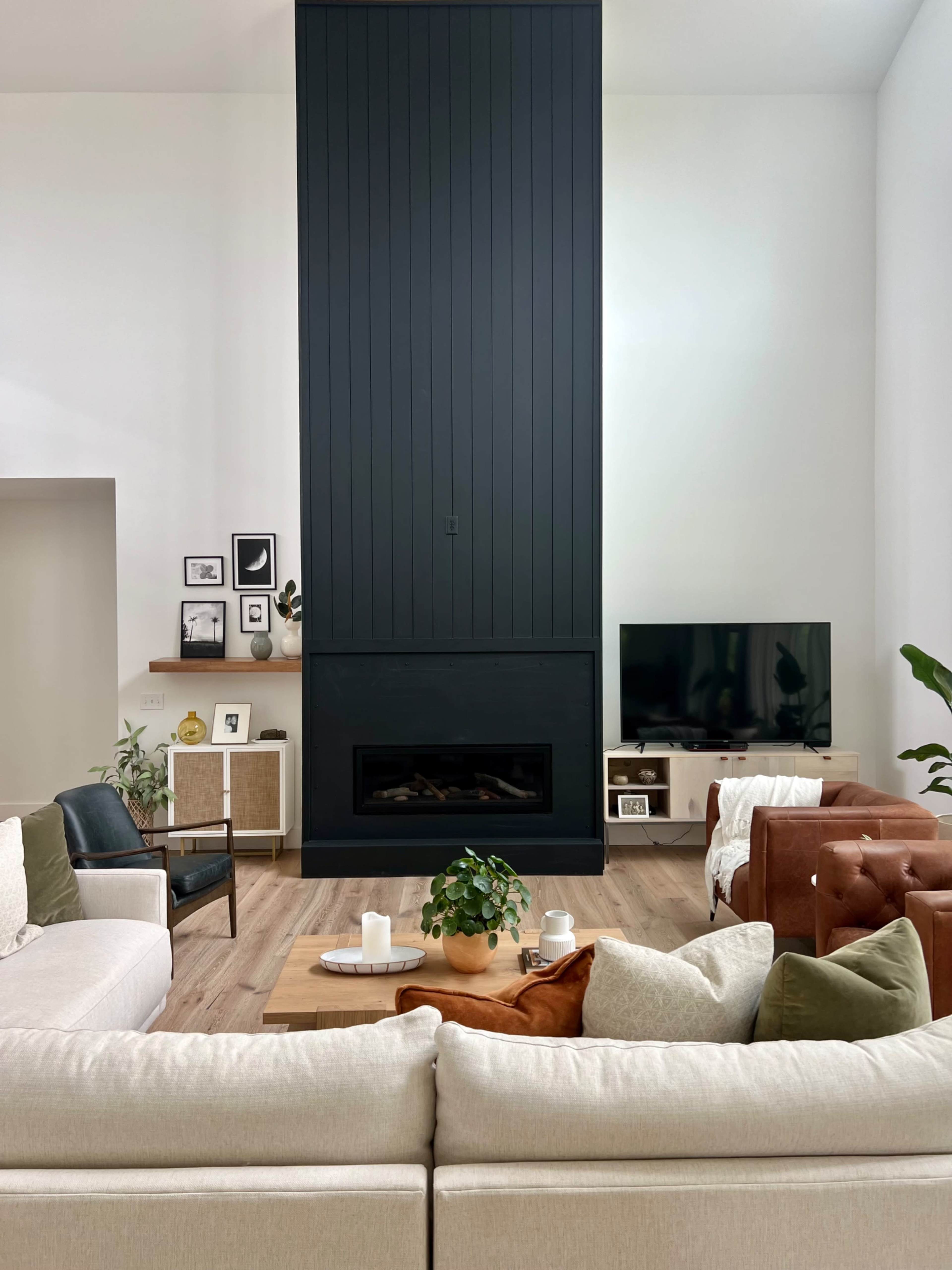 A modern living room features a tall black paneled fireplace, a television stand, and a mix of seating arrangements on wooden flooring.
