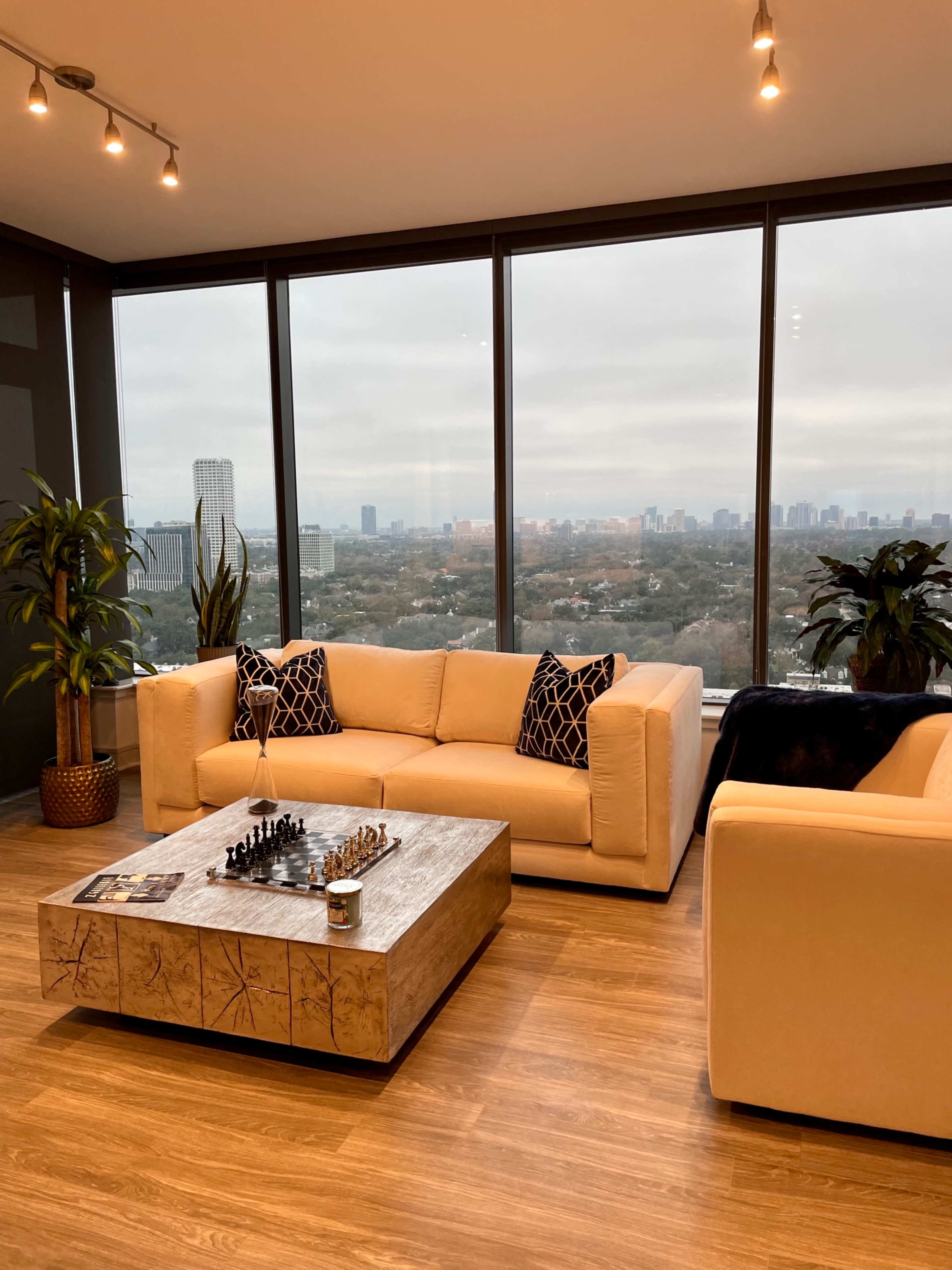 A modern living room features a chess set on a coffee table, surrounded by large windows that offer a view of the city skyline.