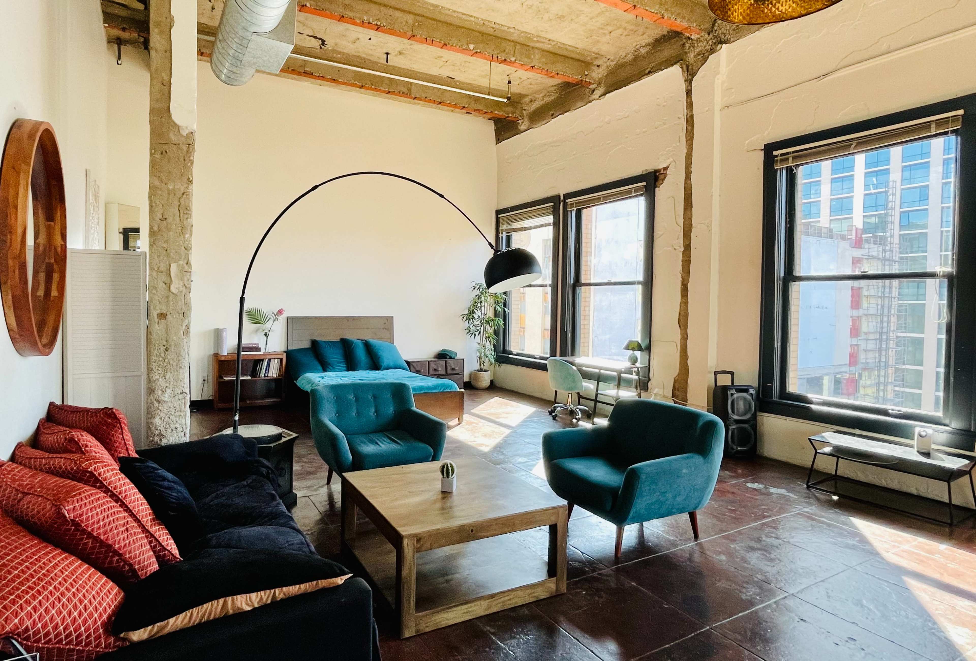 A spacious living room with large windows, featuring comfortable seating, a wooden coffee table, and a tall arc lamp.