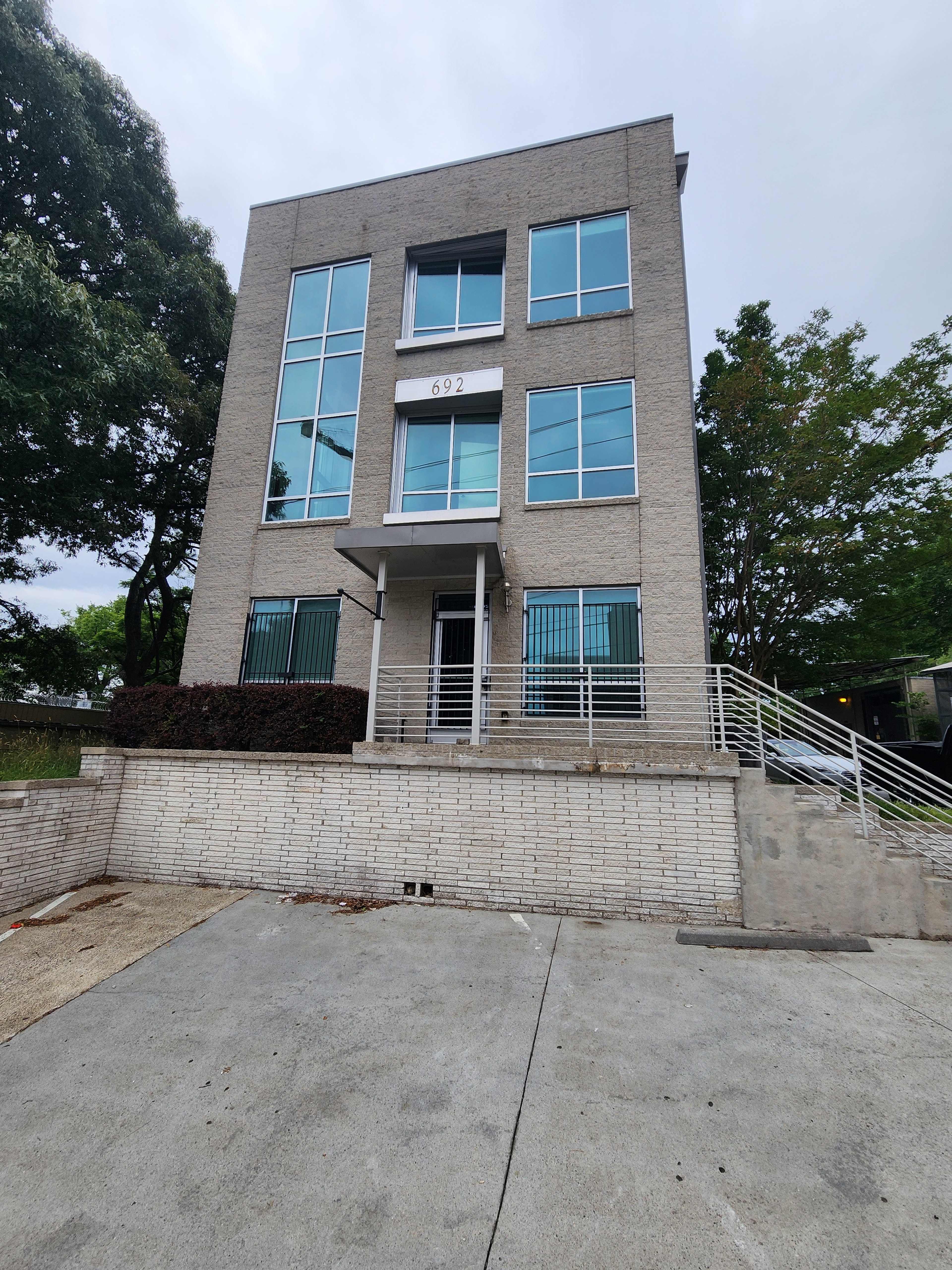 A modern, three-story building with large windows and a ramp leading to its entrance, surrounded by greenery.