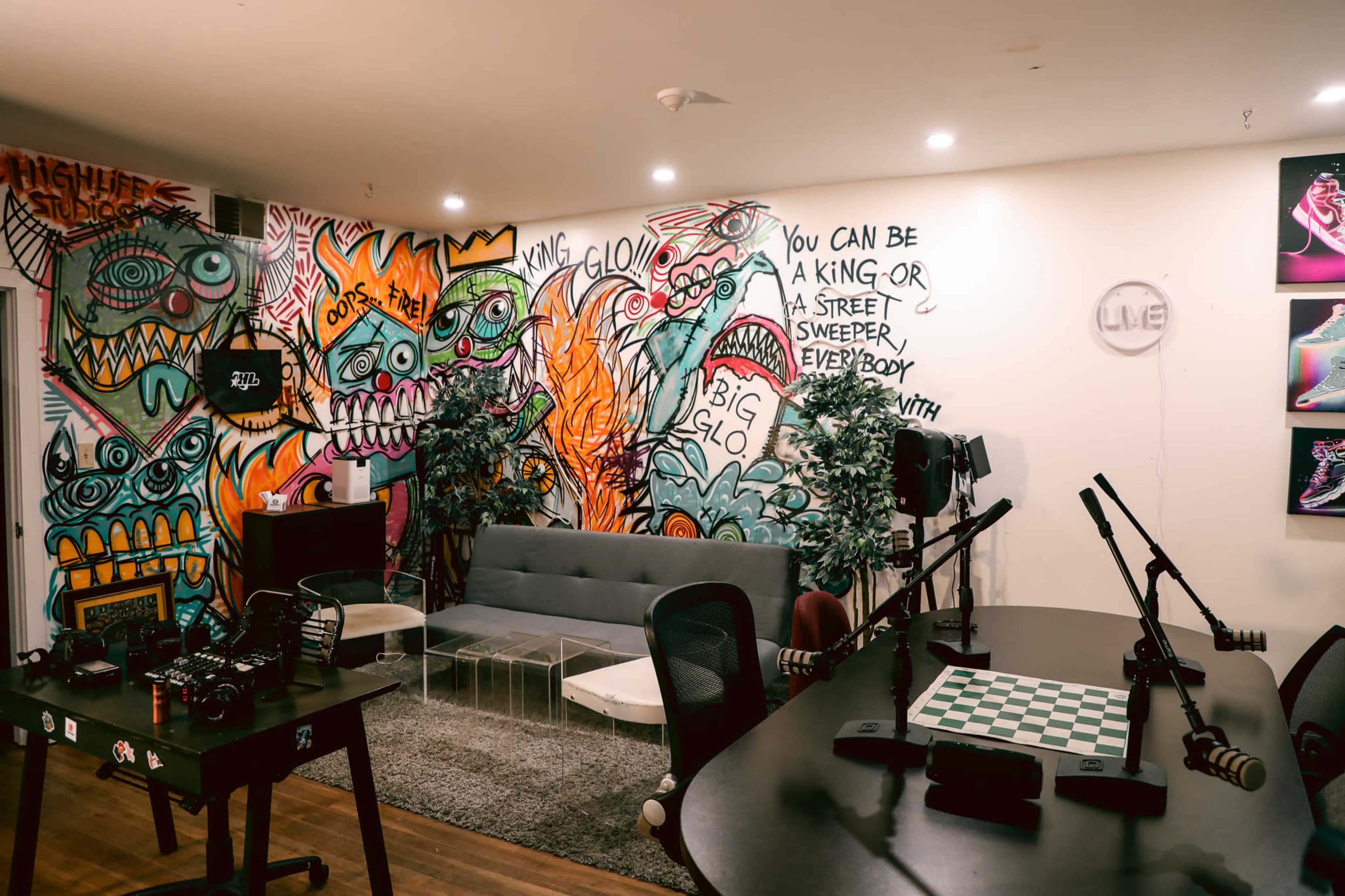 A vibrant creative space featuring a gray couch, a chessboard table, and colorful graffiti on the walls, accompanied by various cameras and microphones.