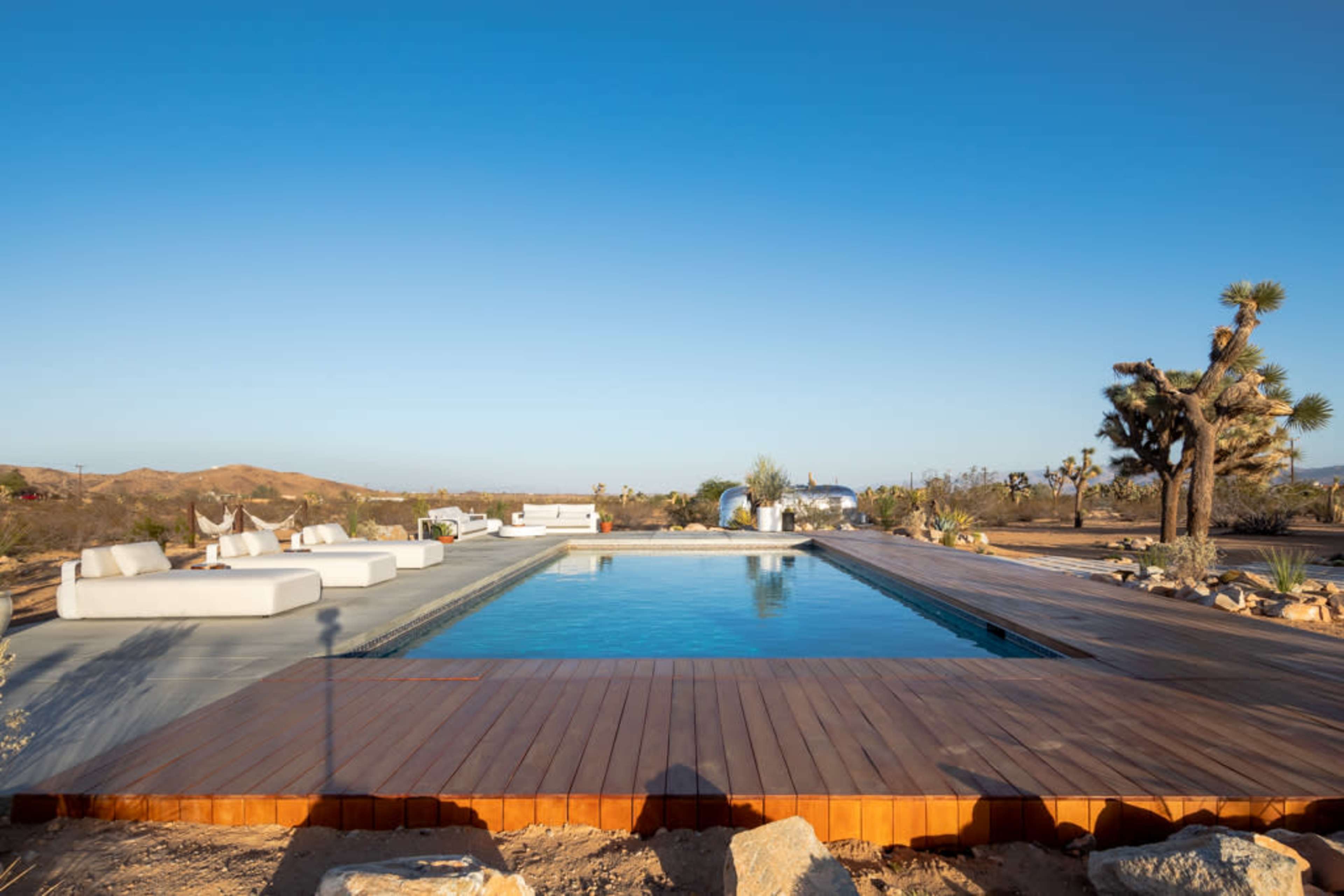 A swimming pool surrounded by a wooden deck and modern outdoor furniture in a desert landscape.