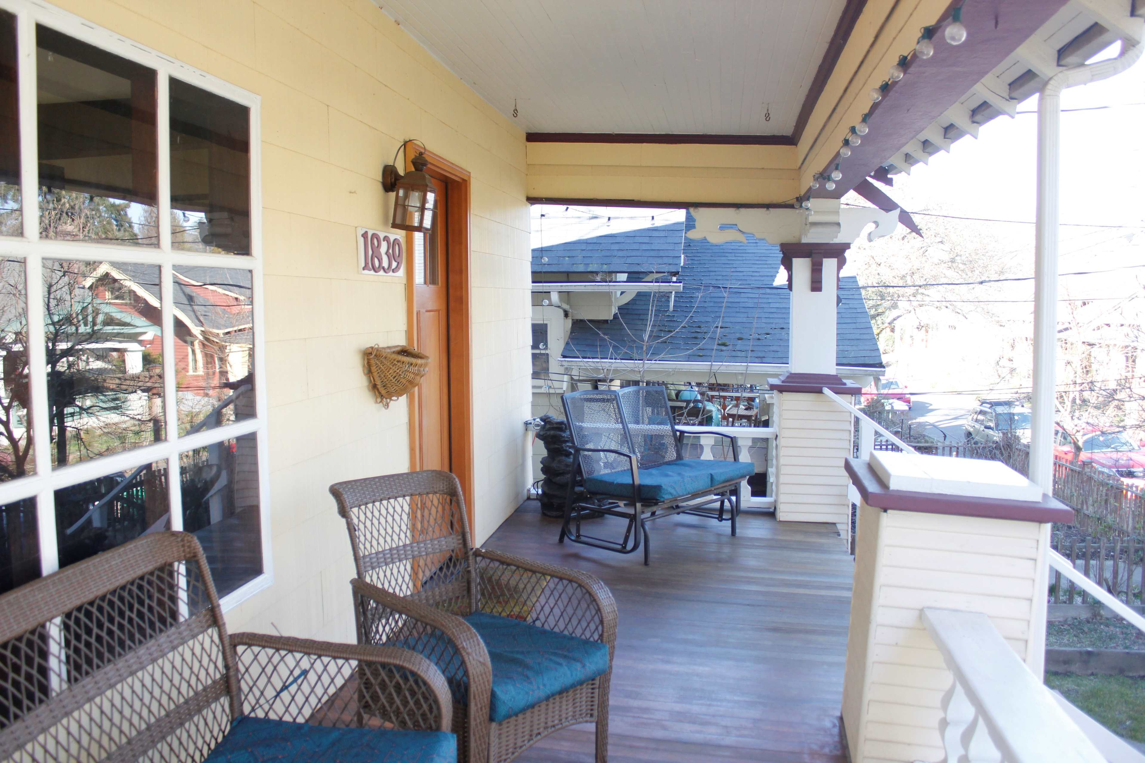 A porch with two wicker chairs, a door labeled "1839," and a view of nearby houses and parked cars.