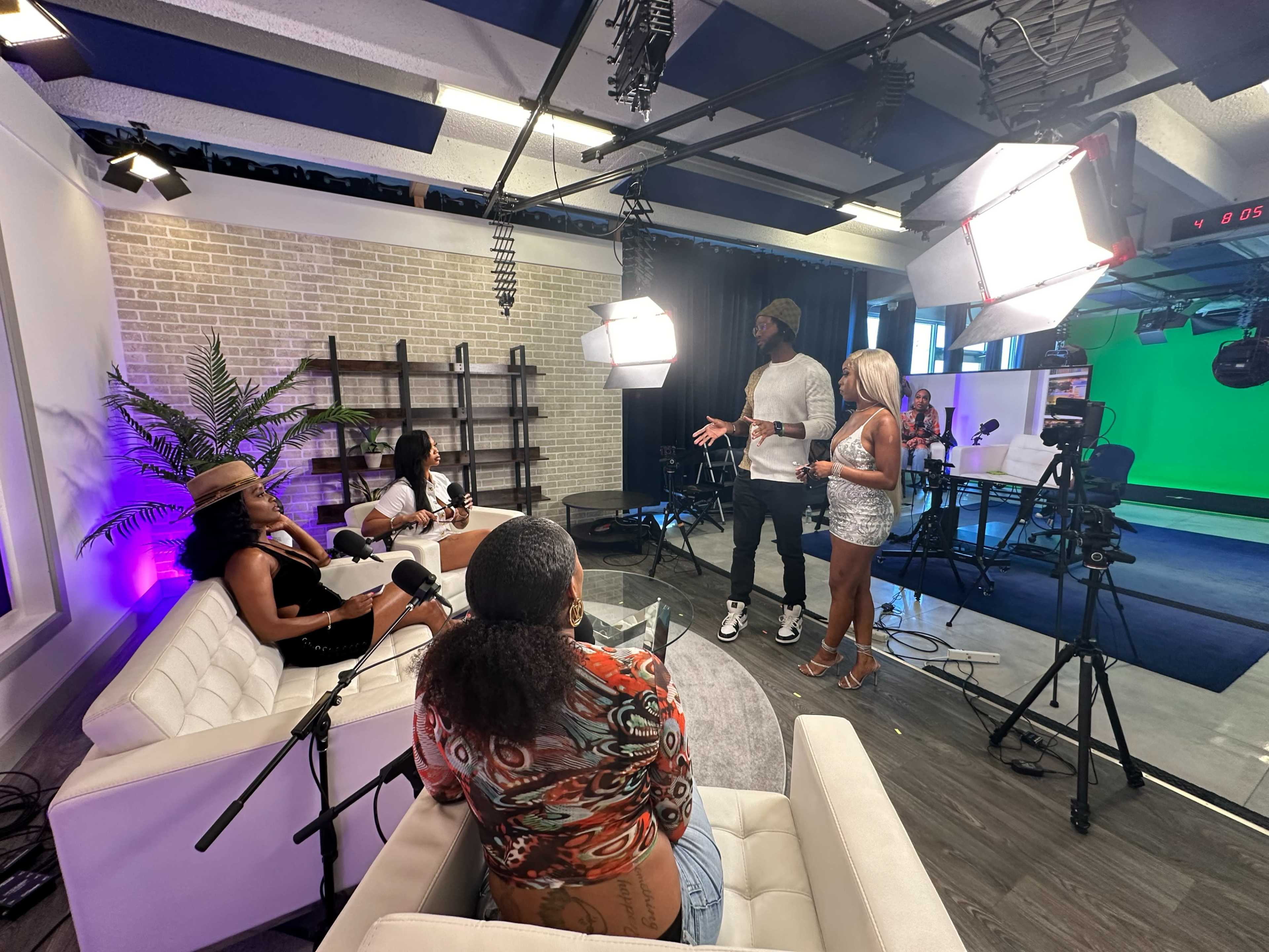 A group of four people engages in a discussion in a modern studio setting with cameras and bright lighting.