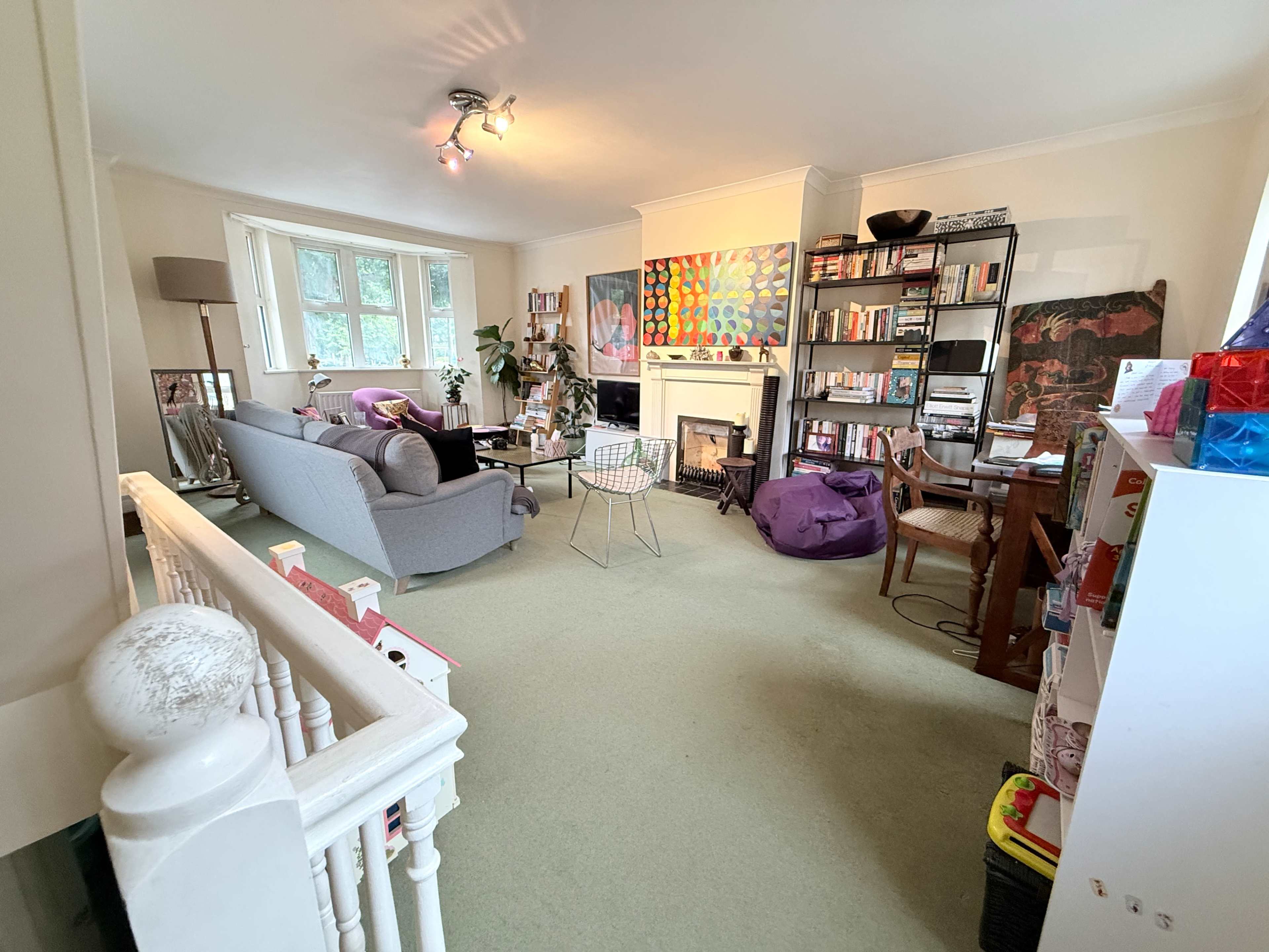 The image shows a living room with a fireplace, bookshelves, a grey sofa, and various decorative items, including a colorful artwork on the wall.