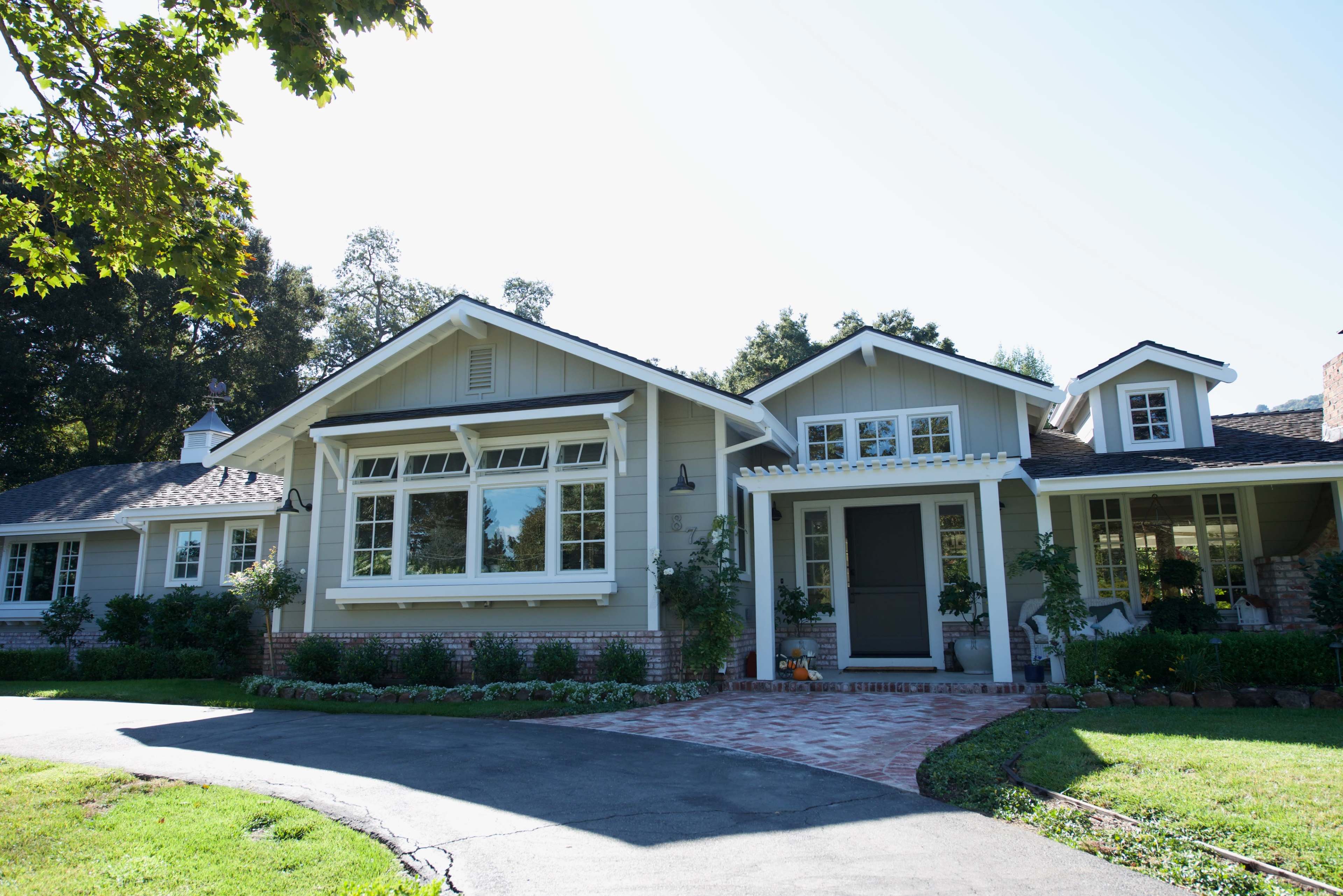 A suburban house with a large front porch, multiple windows, and a neatly landscaped yard.