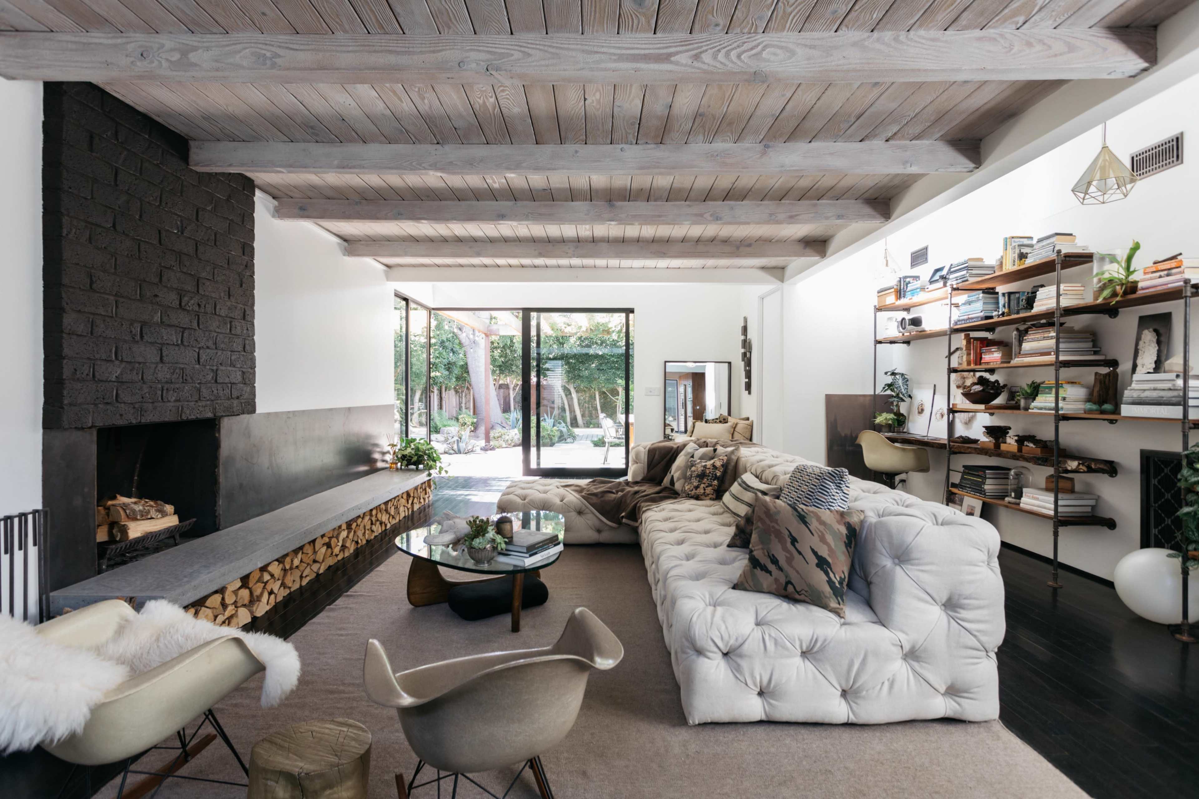 A modern living room with a tufted sofa, a large window overlooking a garden, and a minimalist fireplace.