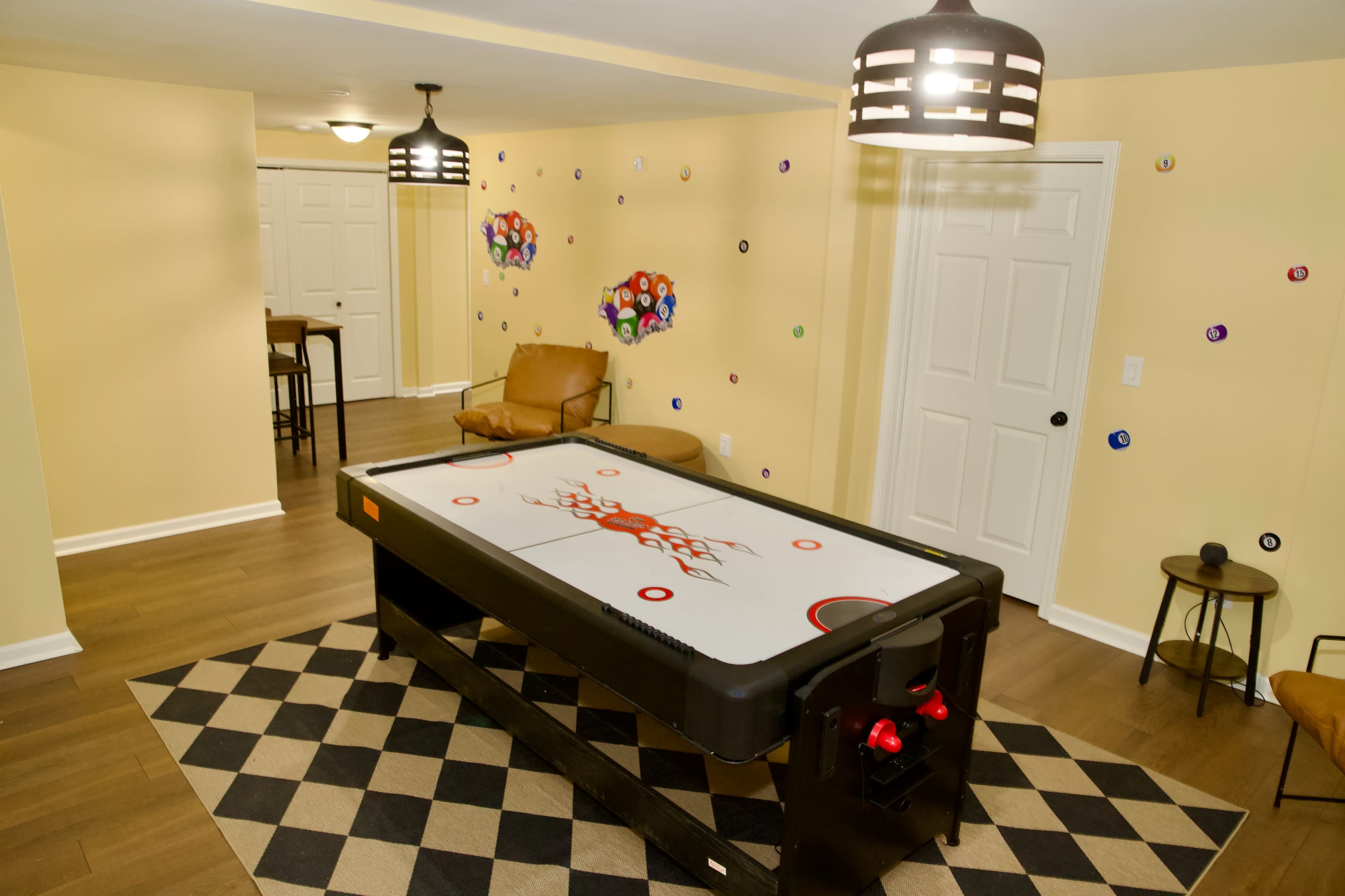 The image shows a game room featuring an air hockey table in the center, surrounded by a patterned rug and decorated walls with colorful circular designs.