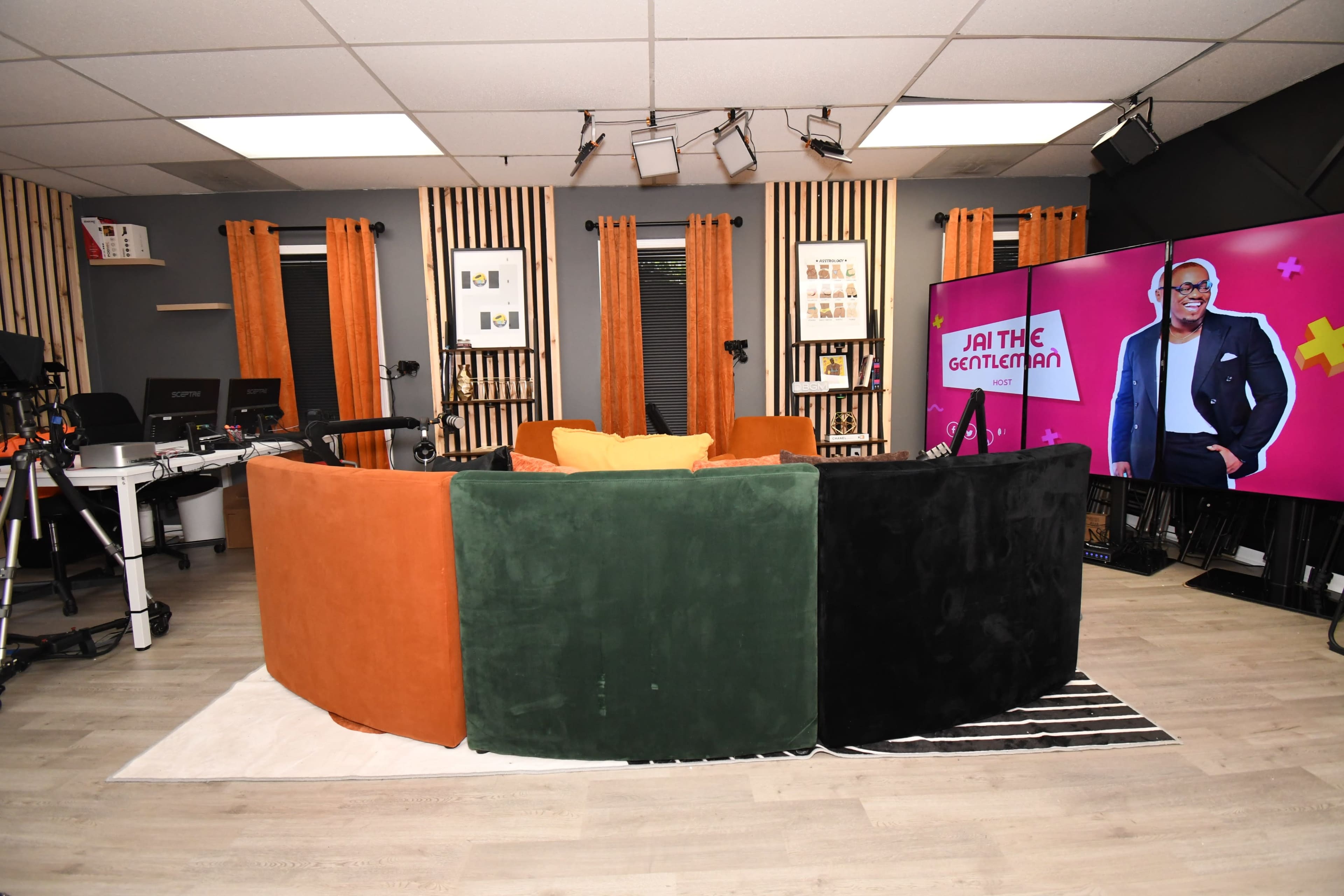 The image depicts a modern studio setup with a curved, colorful couch, a large screen displaying a television program, and professional lighting fixtures.