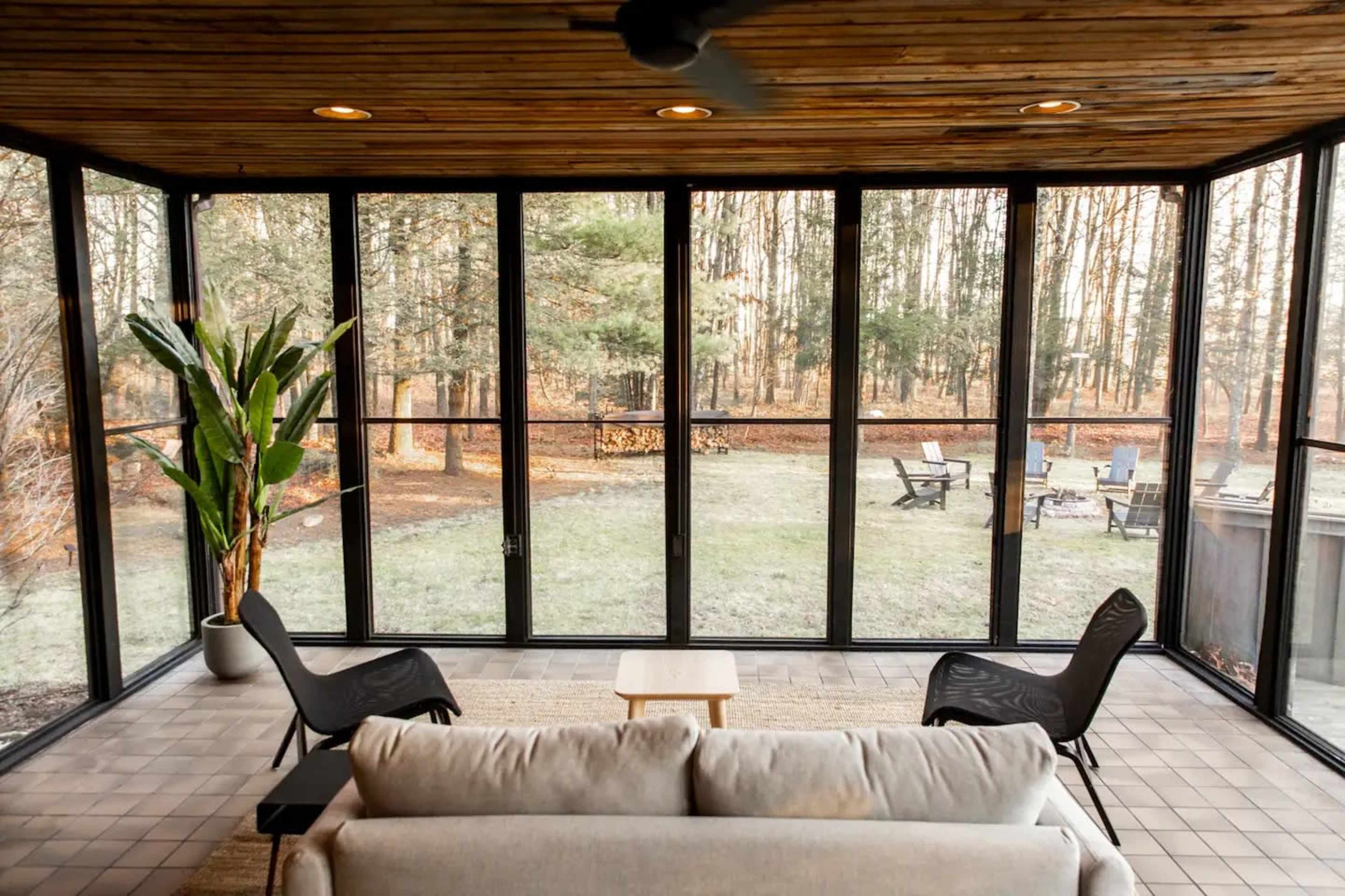 A screened porch with a sofa facing a grassy backyard, surrounded by trees and outdoor seating.