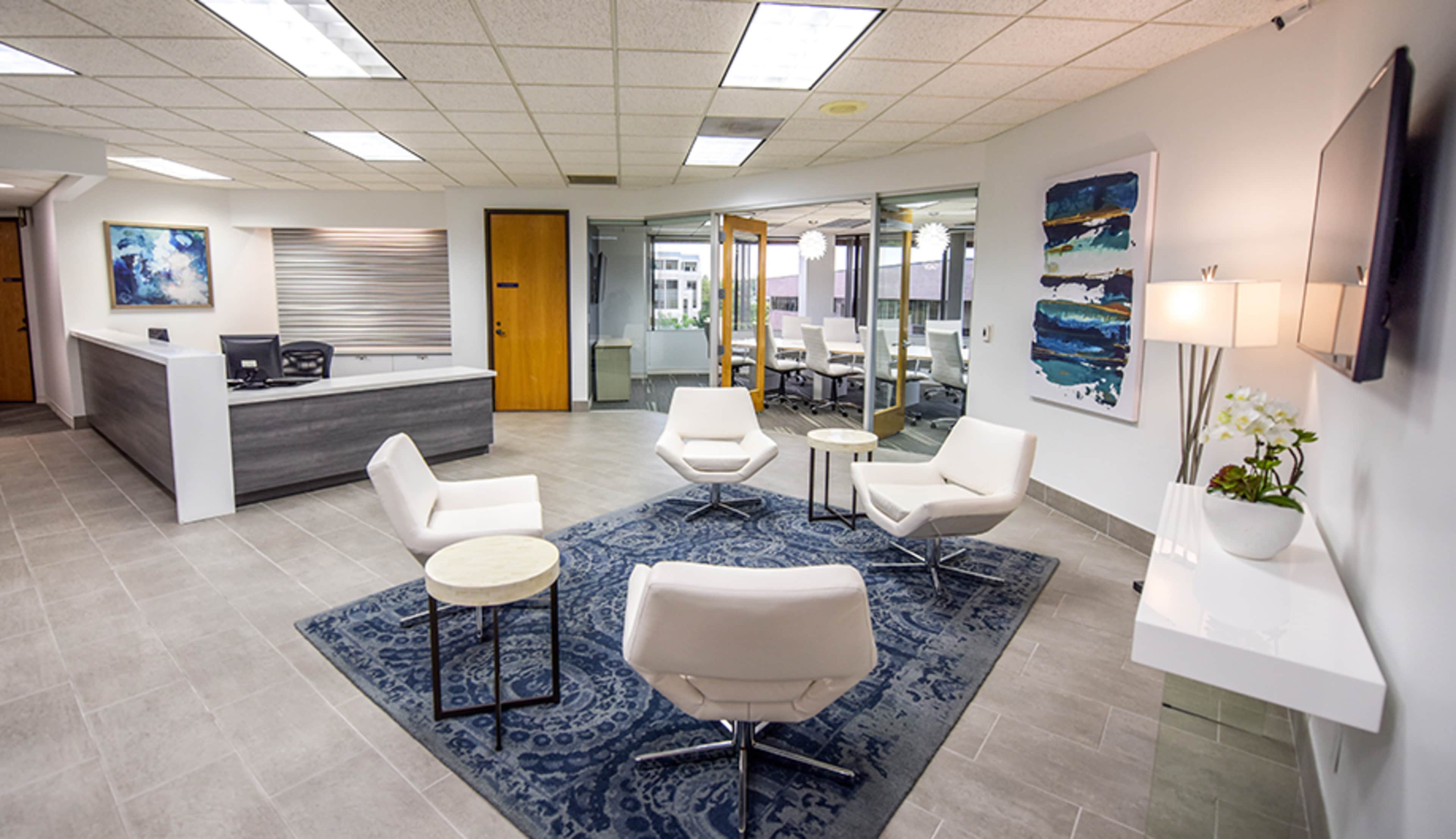 A modern office reception area with white seating, a small coffee table, and artwork on the walls.