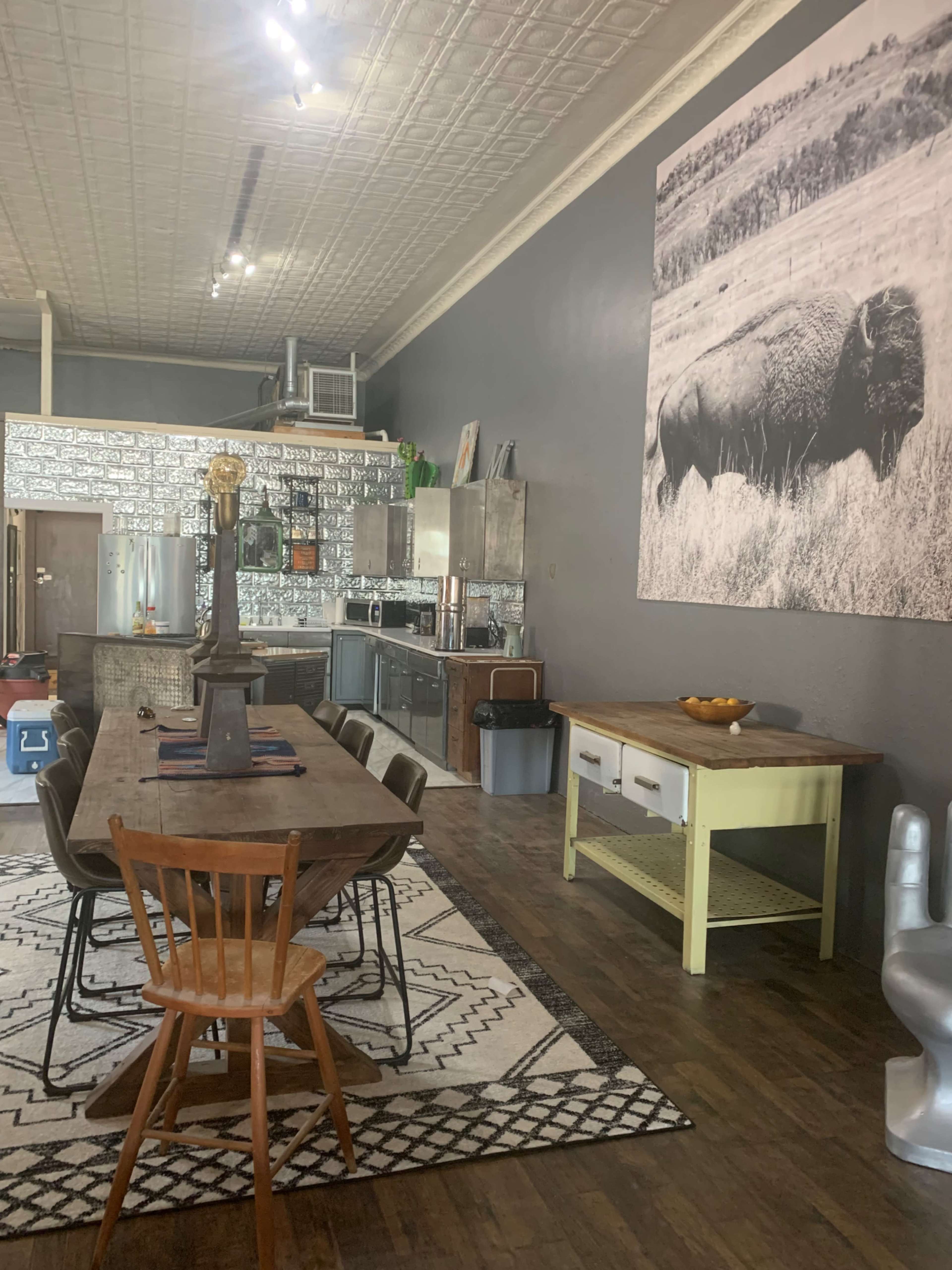 A modern kitchen and dining area featuring a large wooden table with chairs, stainless steel appliances, and a notable black-and-white photograph of a bison on the wall.