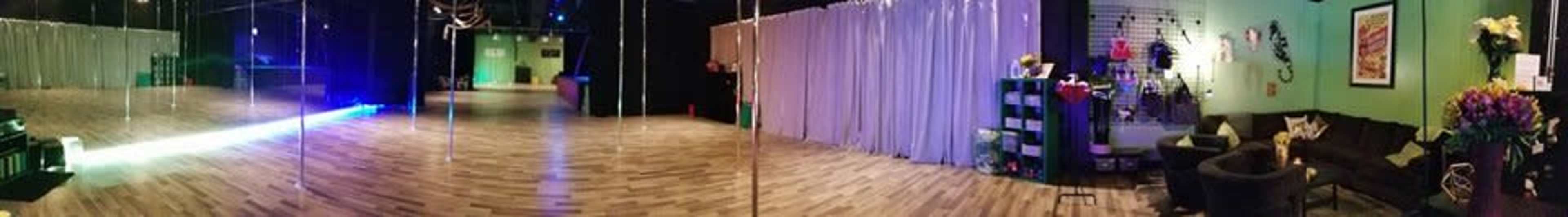 The image shows a spacious indoor studio with polished wooden floors, mirrored poles, and curtains dividing different areas, alongside seating and decorative elements.